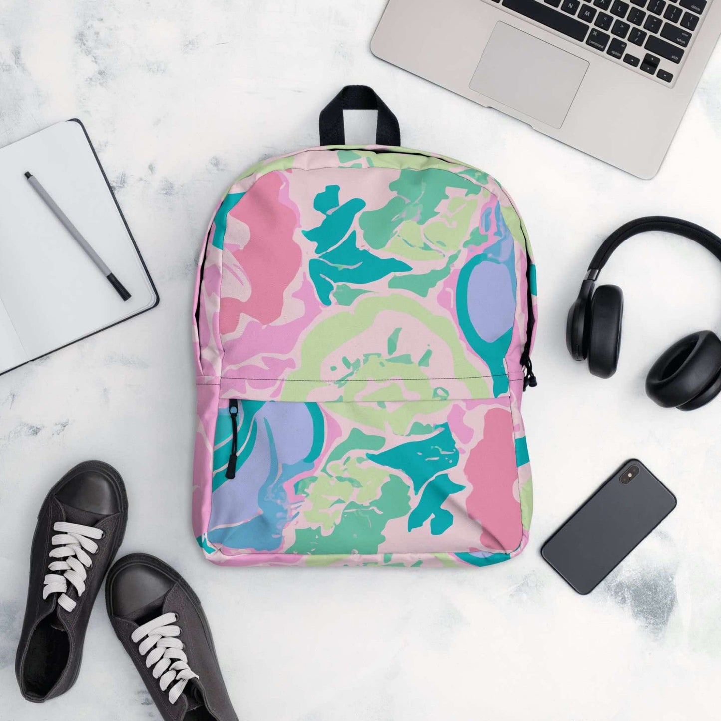 Flatlay of the front of the backpack, surrounded by its possible contents such as a laptop, handphone, headphone, notepad and pen, and even shoes.
