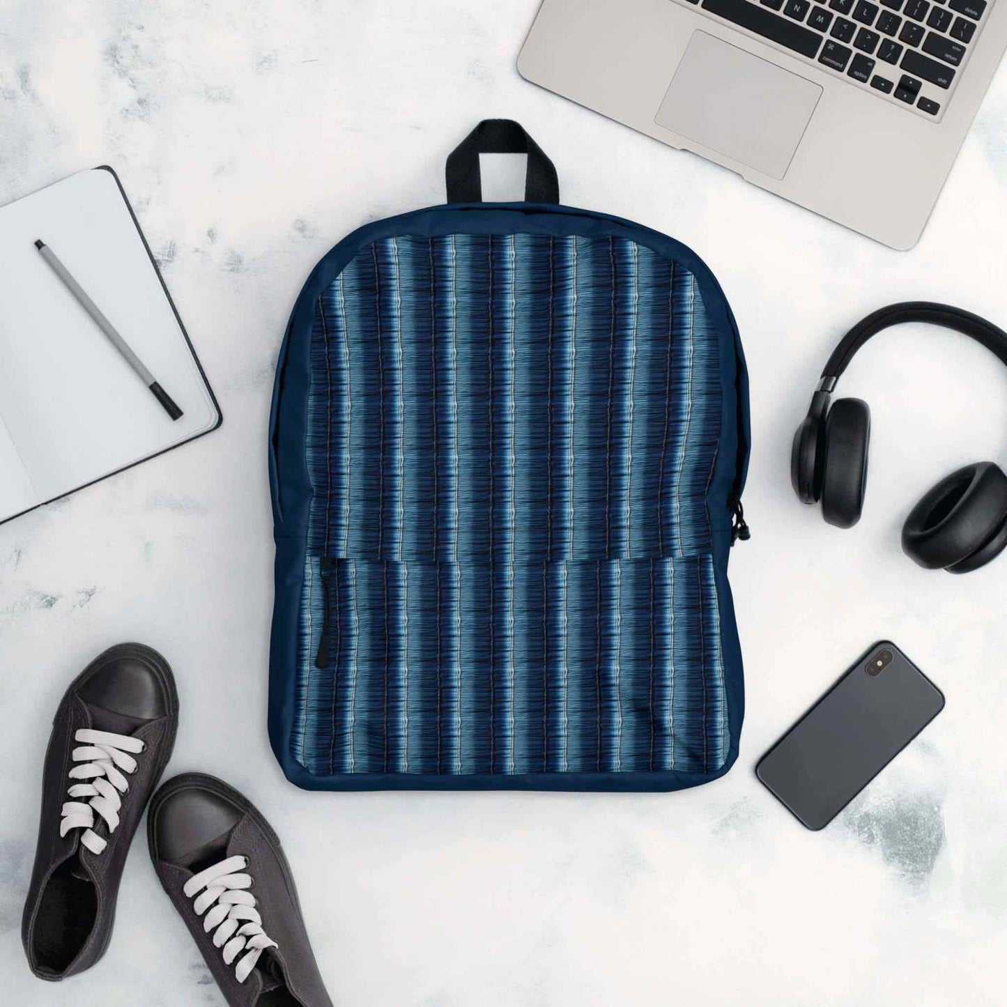 Flatlay of backpack surrounded by its possible contents - laptop, phone, headphone, writing pad, pen and even shoes.
