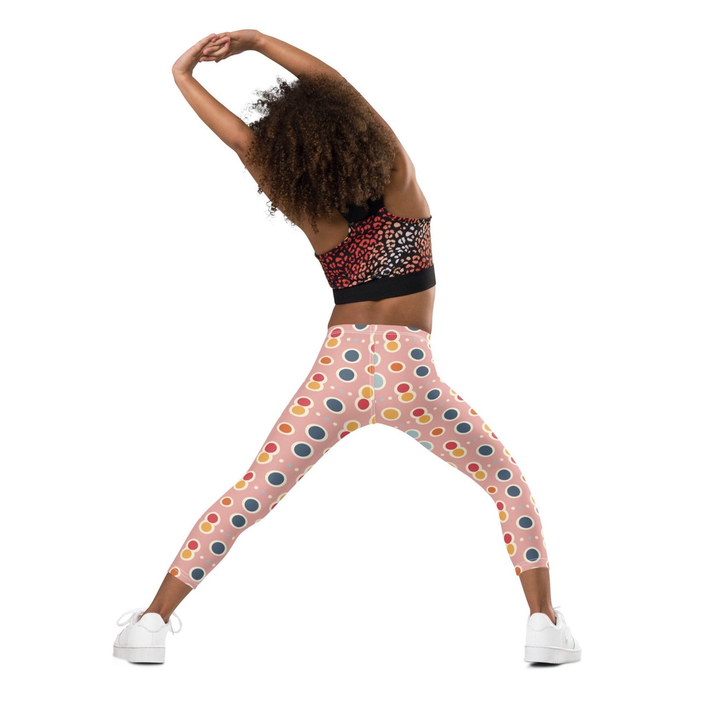 Back view of a black gril wearing a crop top and leggings which features a playful pattern of pastel and white circles on a pink background. The girl has her hands and legs stretched out as she exercises.
