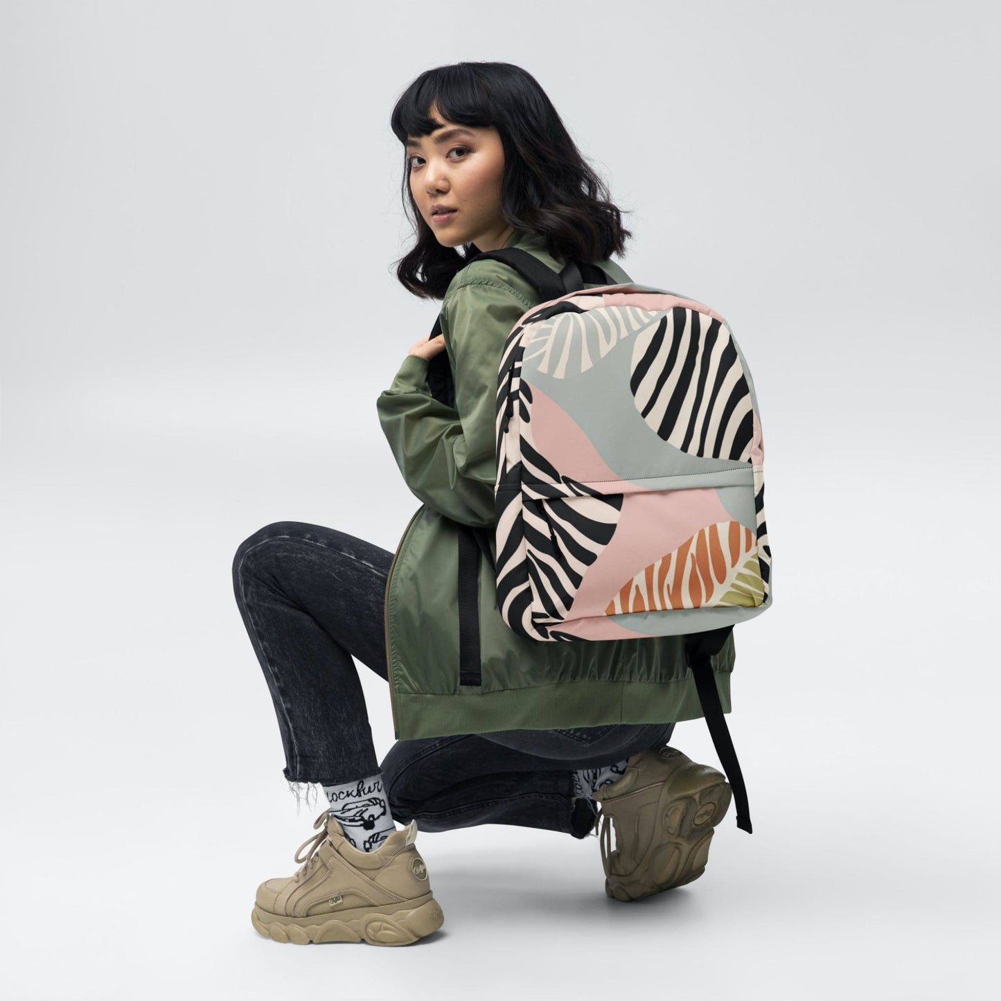 A zebra print backpack on the back of a girl. The backpack features a zebra inspired design with blacks, soft pink, soft green and tan colours.