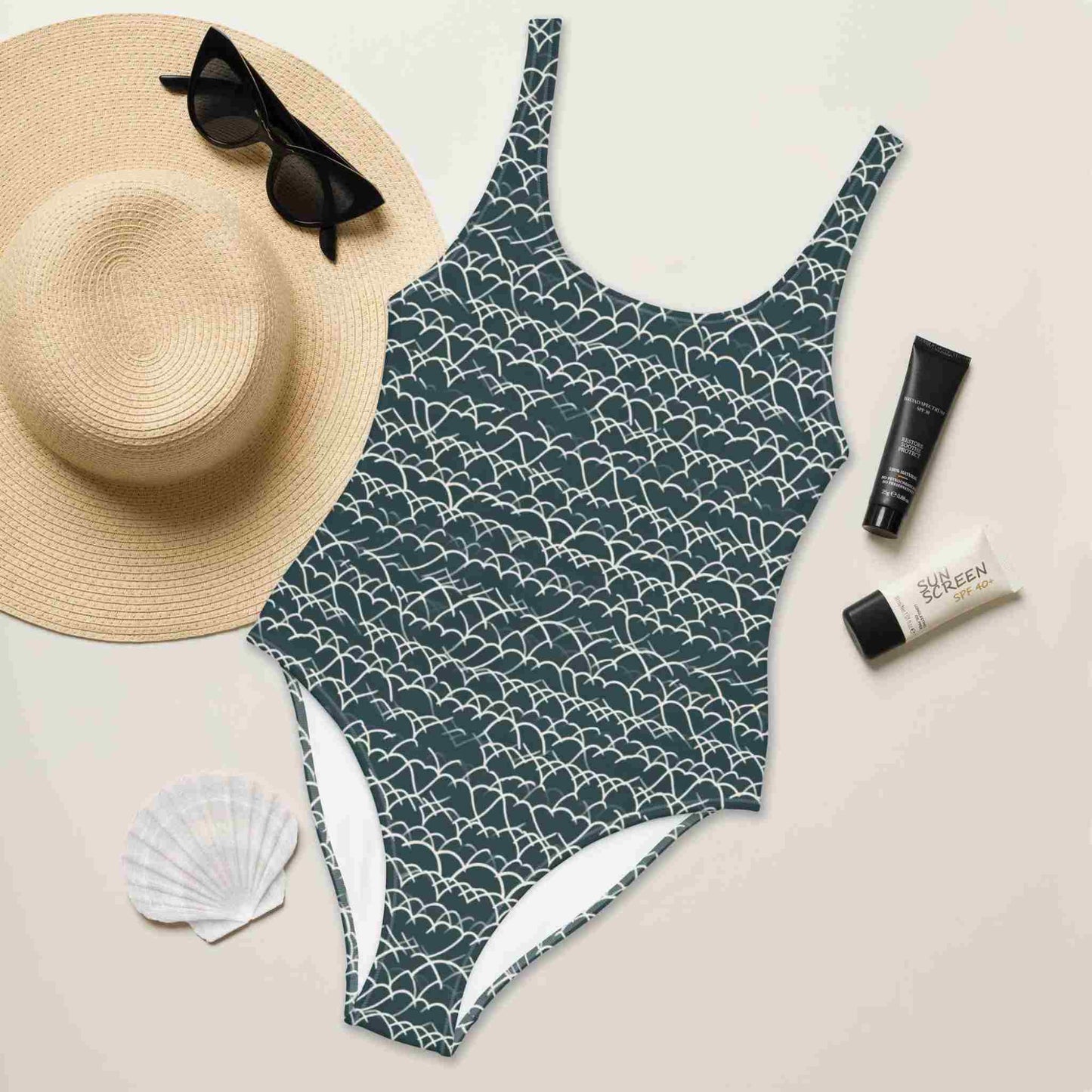 Flat lay of a blue and white pattern swimsuit (one piece) which features a white geometric white design that dances across a blue background, front side up, surrounded by a hat, sunglass, sea shell and sun lotion.