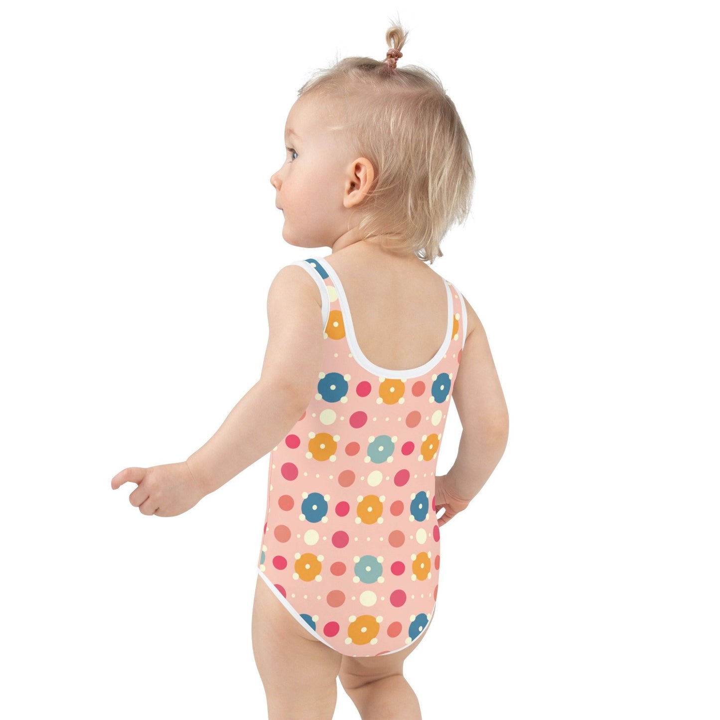 Cute infant swimsuit, suitable for kids in general, features a playful pattern of pastel and white circles on a pink background, worn by an infant, with her back to the camera. White background.