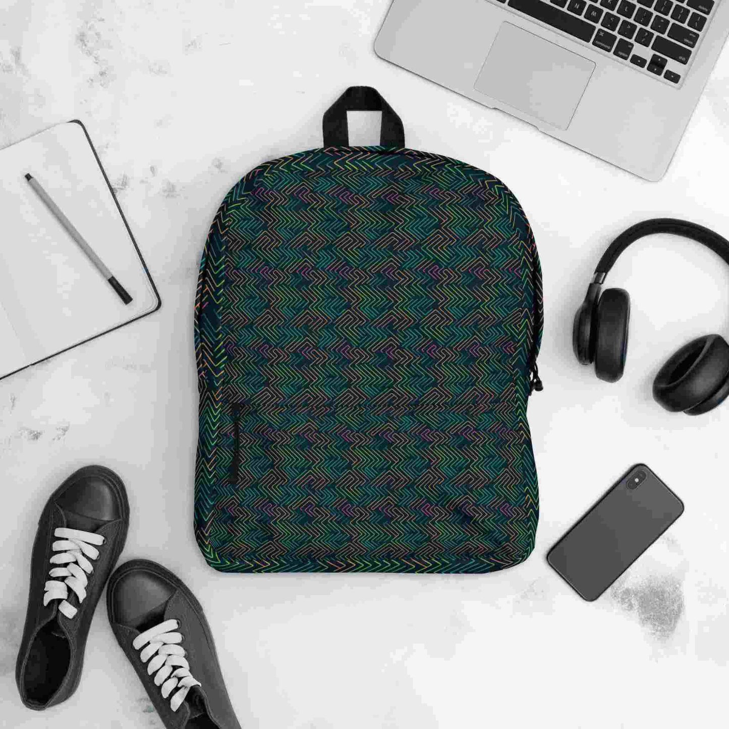 Flatlay of a printed backpack, featuring a dark neon electrical circuit design, surrounded by items it could possibly contain, including a laptop, handphone, headphone, note pad and pen, and even shoes.