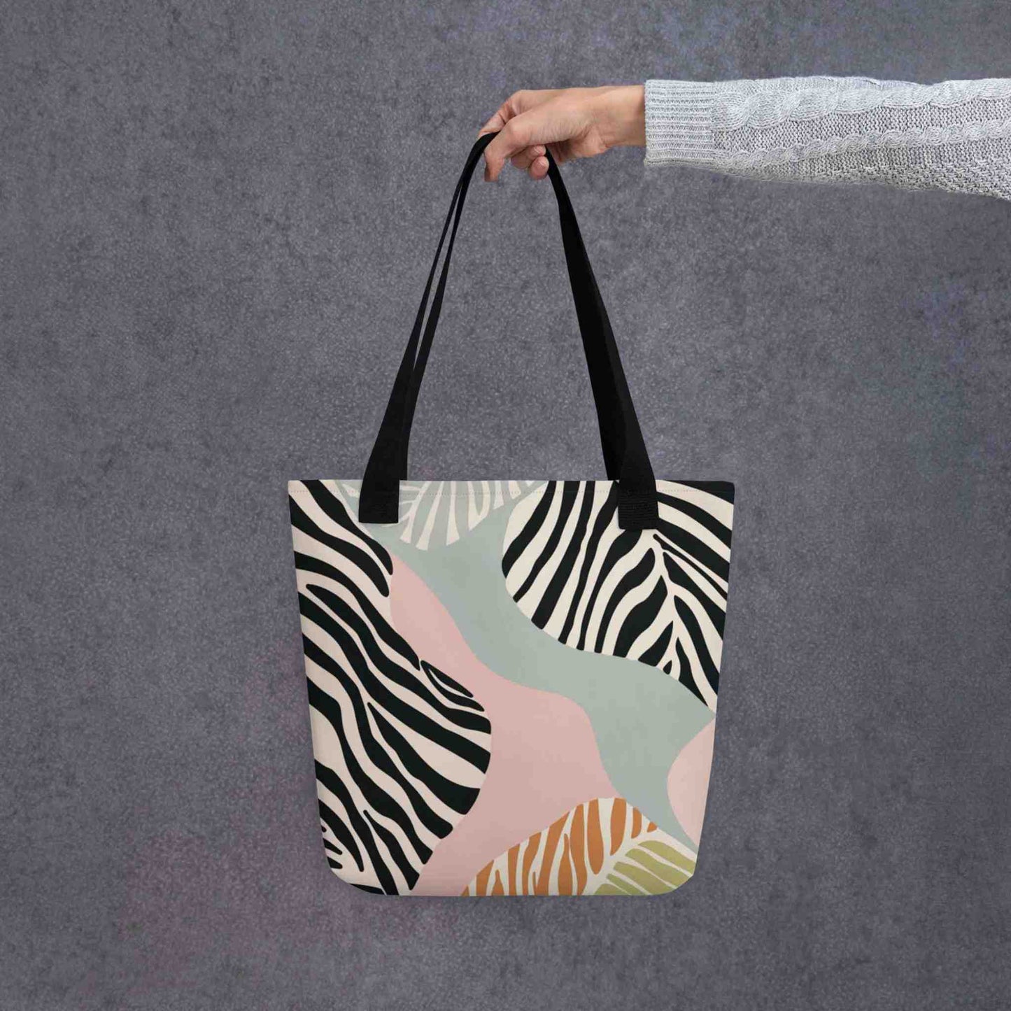 Zebra print tote bag with black handles, in a colourful and avant garde zebra inspired design, held in a lady's hand. Dimension 15x15 inches. Grey background.