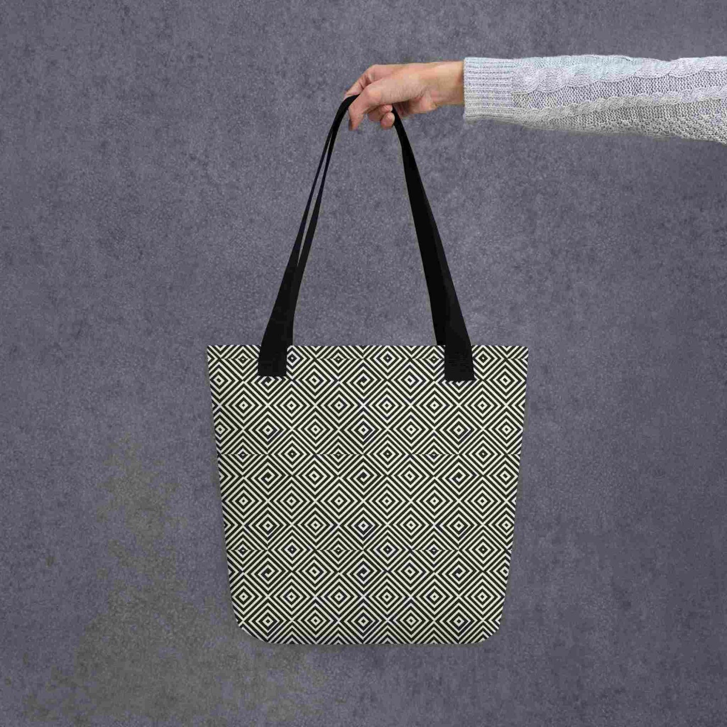 Diamond pattern tote bag with black handle, a mesmerizing black and white geometric look, held in a lady's hand against a grey background.