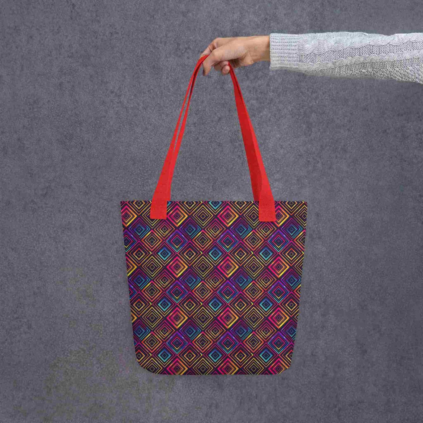Fashion tote bag with red handles, which features a neon tapestry design in a sophisticated blend of colors, held by a lady's hand. Dimension 15x15 inches. Grey background.