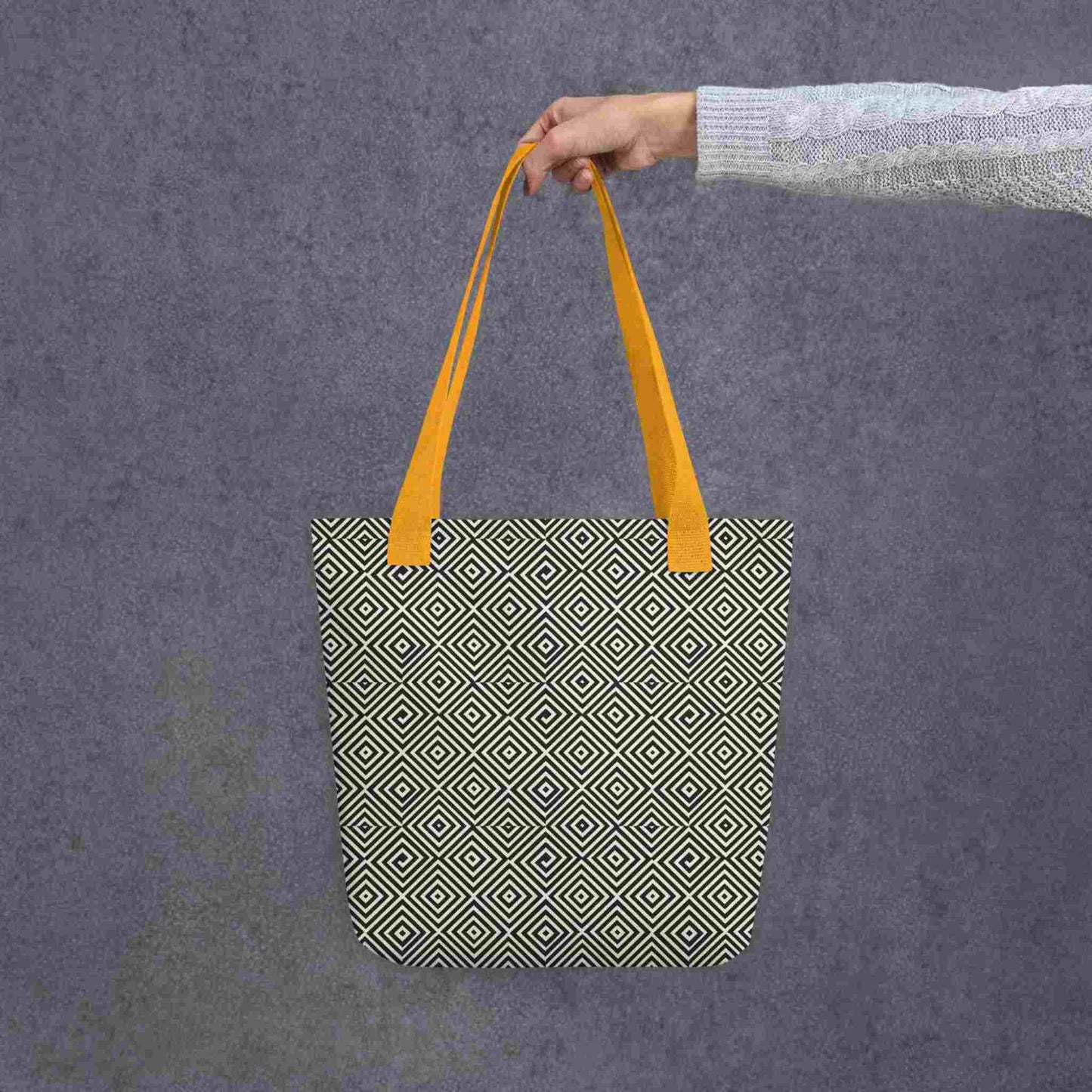 Diamond pattern tote bag with yellow handle, a mesmerizing black and white geometric ook, held in a lady's hand against a grey background.