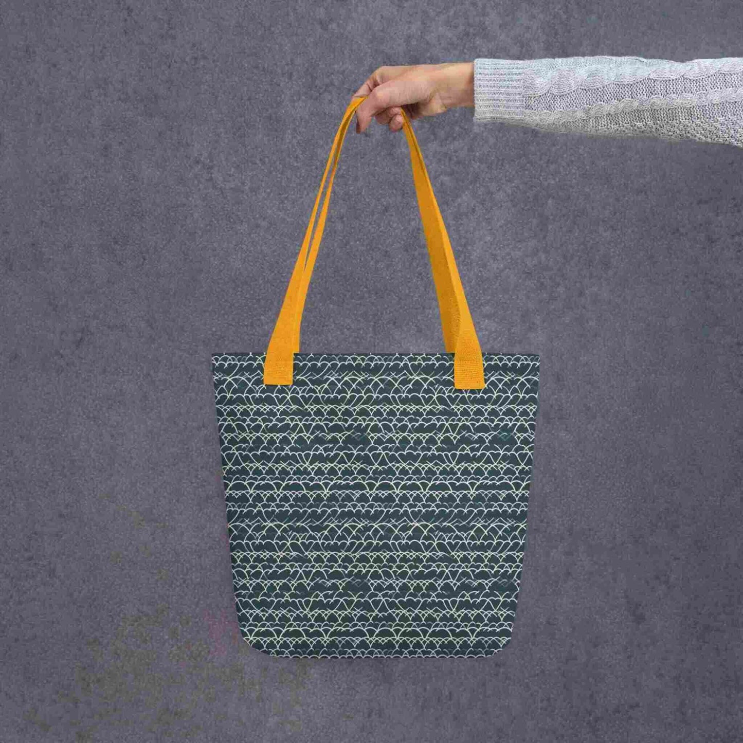 Blue Tote with White Geometric Lace with yellow handles, held by a lady's hand. Dimension 15x15 inches. Grey background.