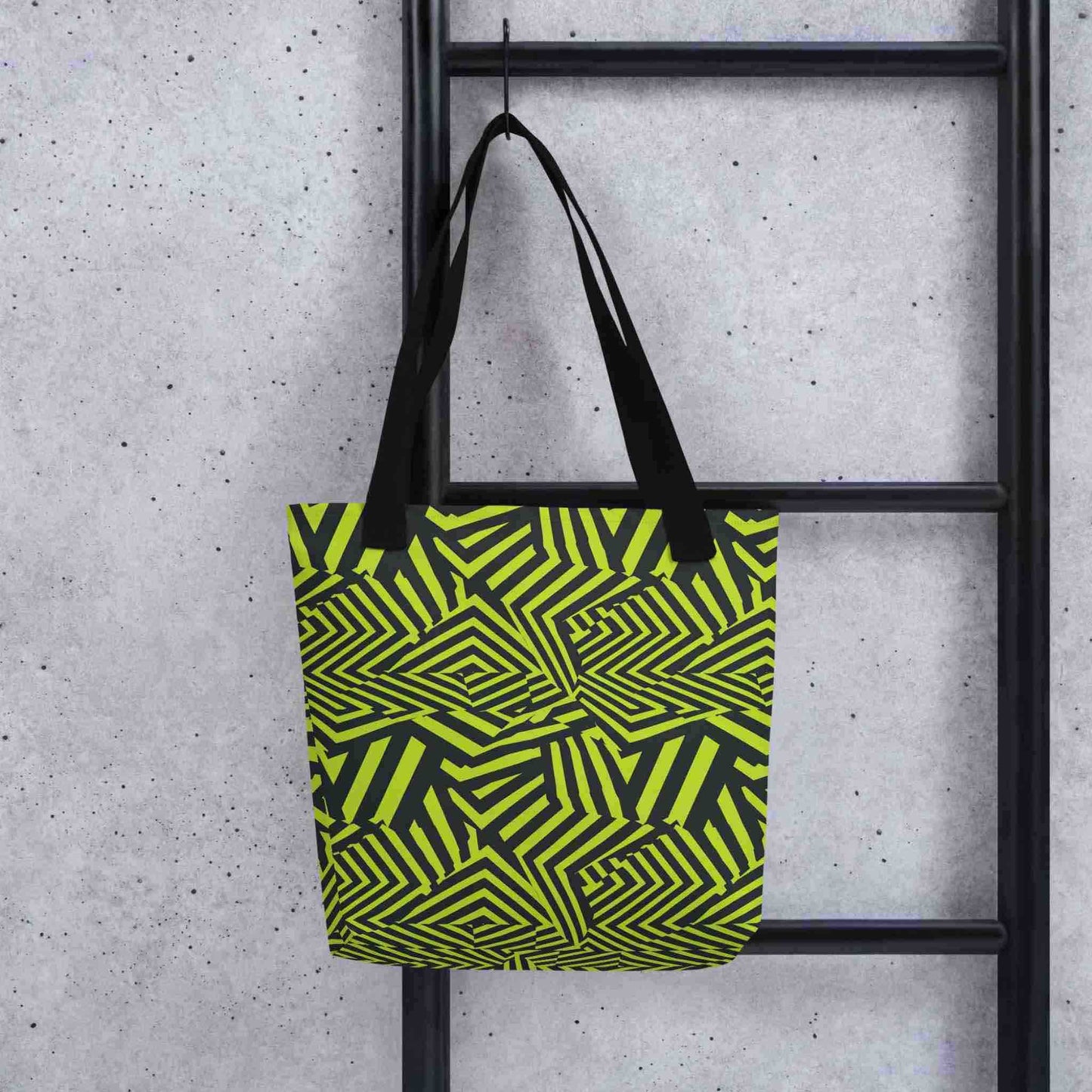 An avant garde tote bag with black handles, which features bold black and green op art illusion, hooked onto a black ladder. Size is 15x15 inch. Grey background.