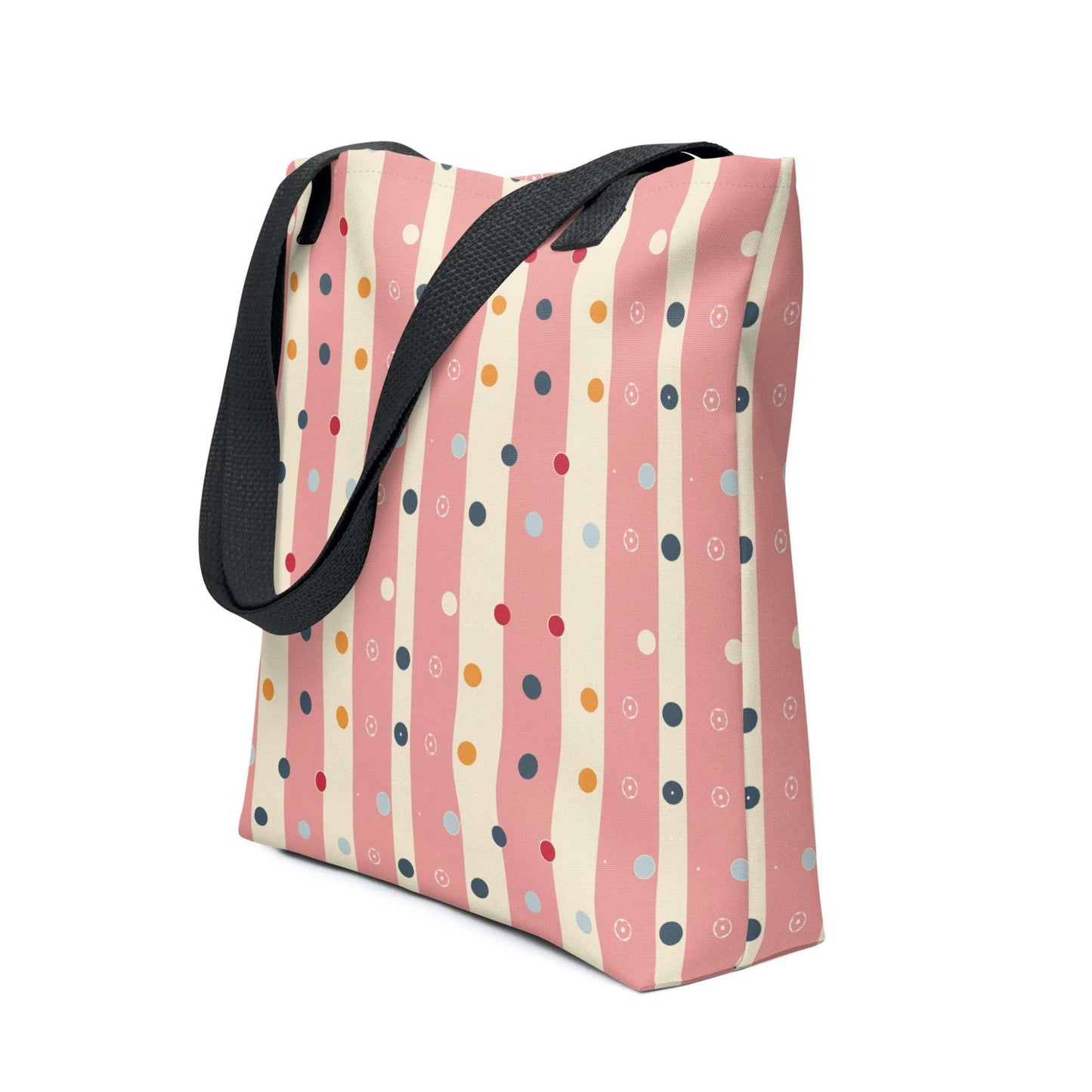 Pink striped tote bag with black handles, which features pink and beige stripes with colourful pokka dots, shown in side view.. White background.