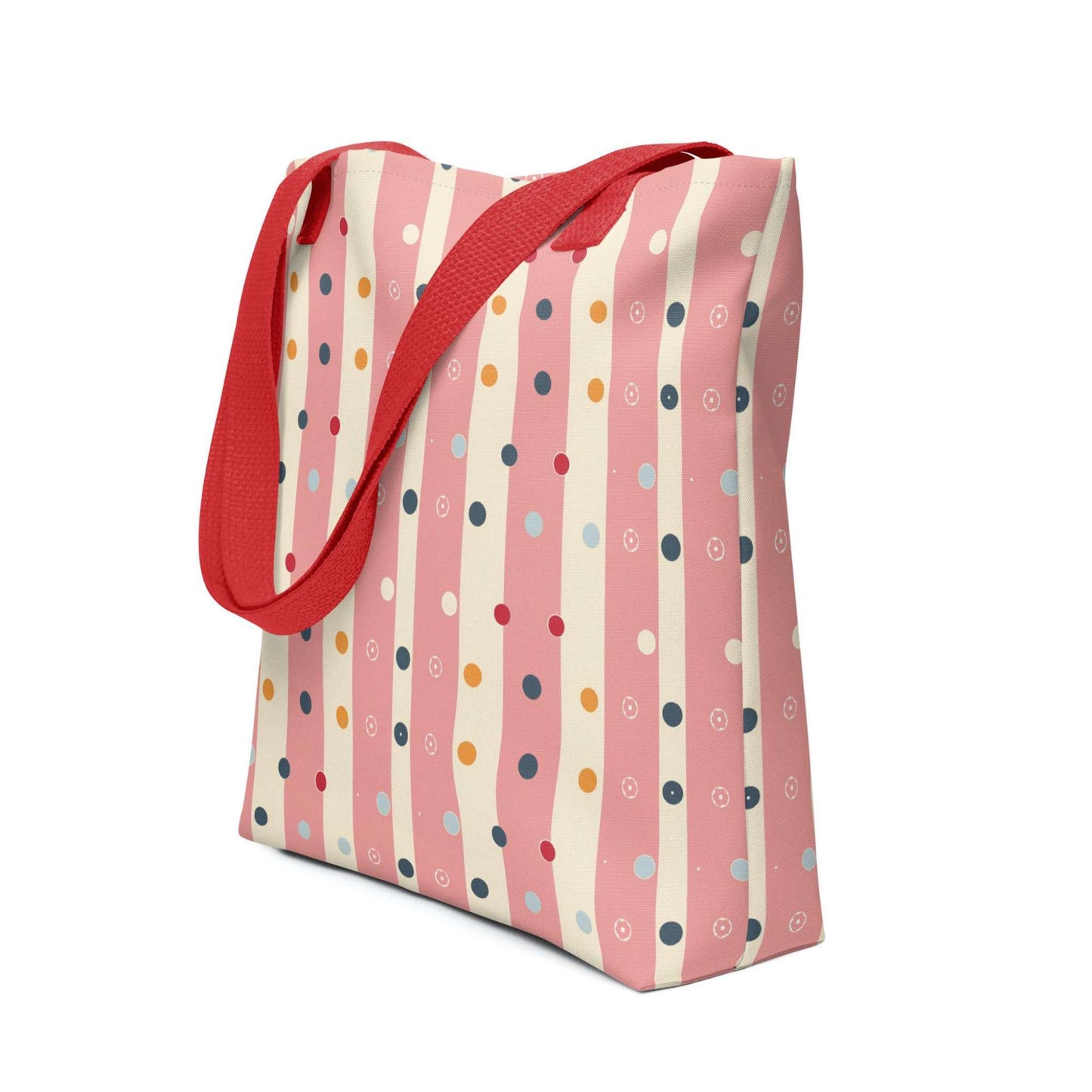 Pink striped tote bag with red handles, which features pink and beige stripes with colourful pokka dots, shown in side view.. White background.