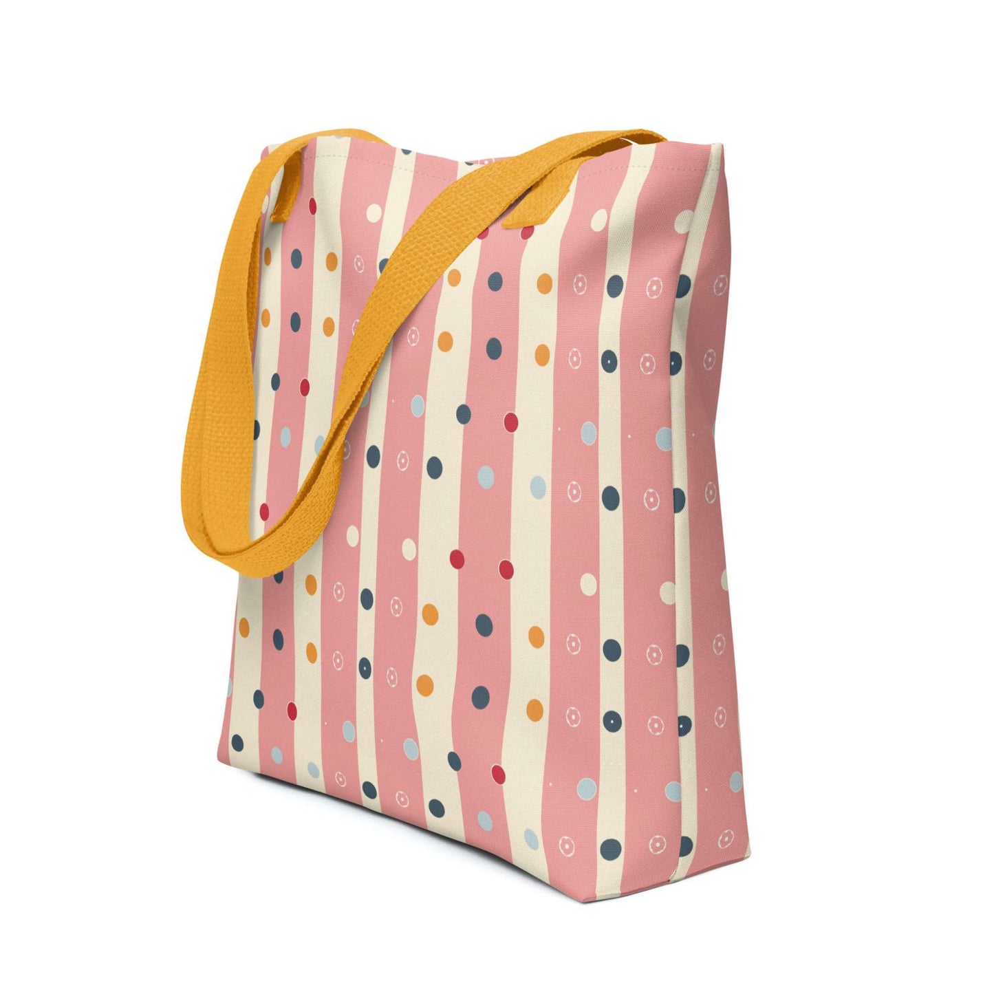 Pink striped tote bag with yellow handles, which features pink and beige stripes with colourful pokka dots, shown in side view.. White background.