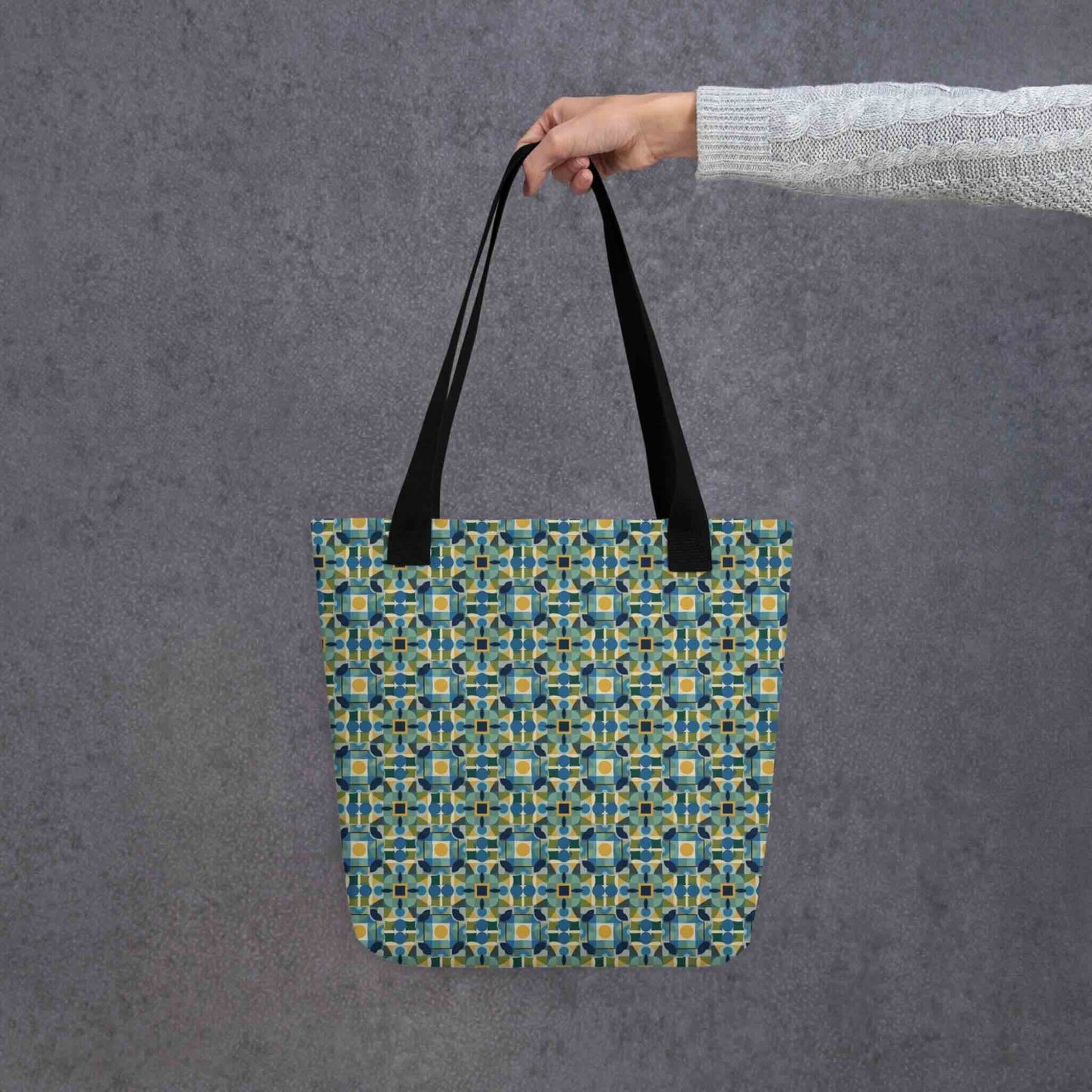 Elevate your style with the TILEWAVE Abstract Tote Bag, featuring a vibrant geometric tile pattern in modern retro hues. Perfect for daily essentials, this 15" x 15" polyester tote bag combines playful structure with sophisticated charm. Black handle. Held in a hand. Grey background.