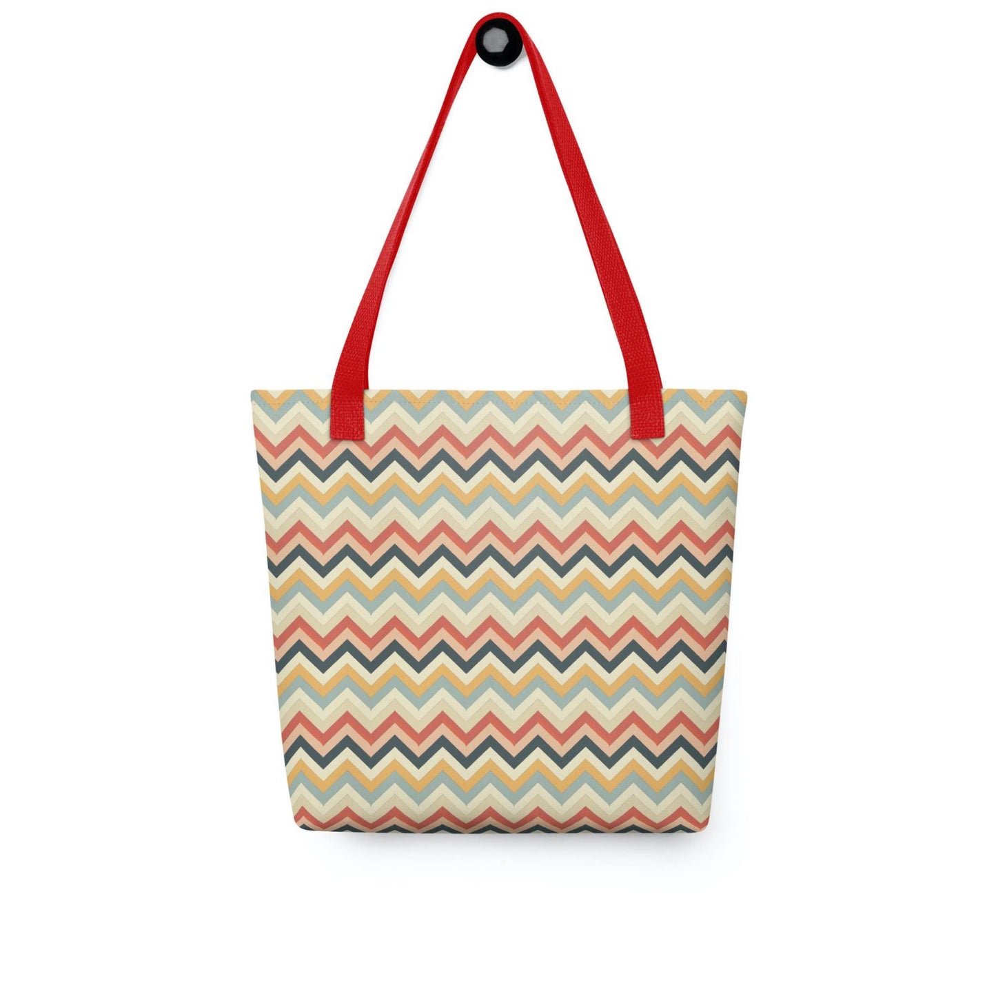 Zig zag tote bag with red handles, in a multicoloured pattern of Zig Zag lines, hanging on a white wall. Dimension 15x15 inches. White background.