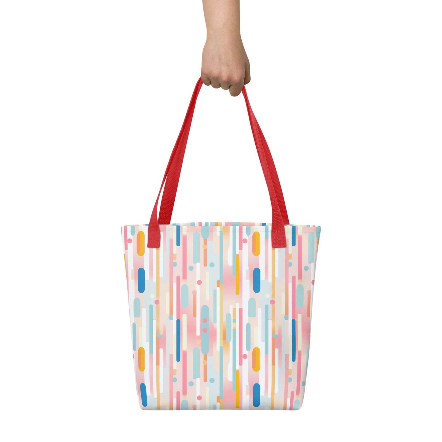 Light pink tote bag with red handles, which design is abstract vertical lines of pastel pink and other pastel shades, held in a hand against a white wall. Dimension 15x15 inches.