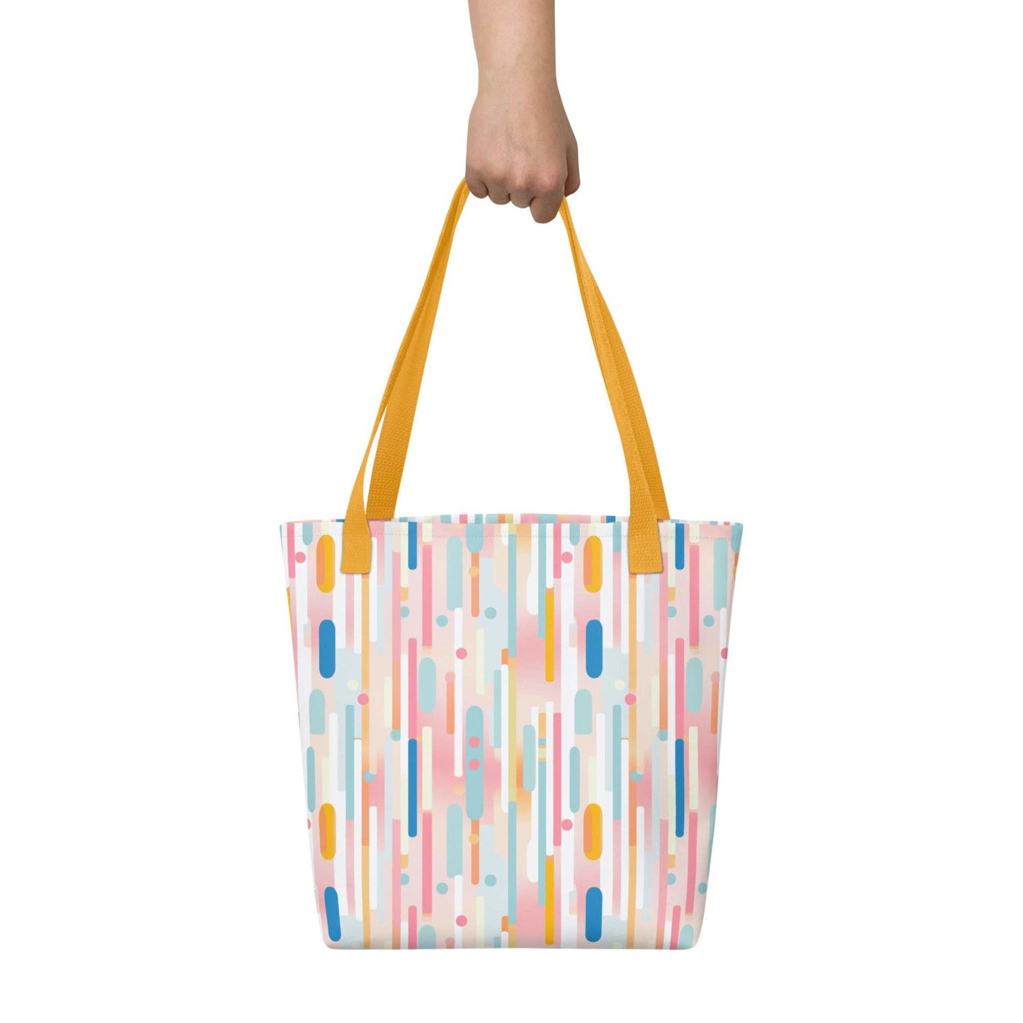 Light pink tote bag with yellow handles, which design is abstract vertical lines of pastel pink and other pastel shades, held in a hand against a white wall. Dimension 15x15 inches.