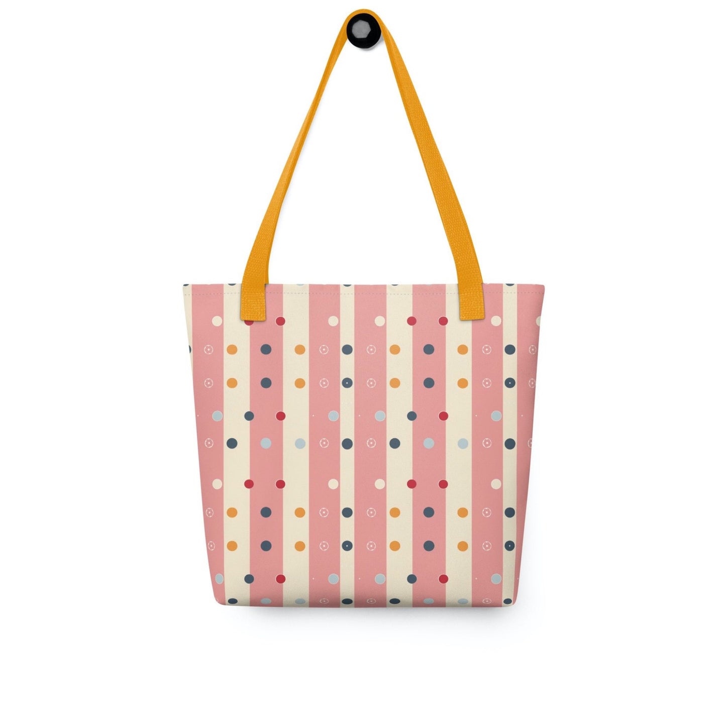 Pink striped tote bag with yellow handles, which features pink and beige stripes with colourful pokka dots, hanging on a white wall. Dimension 15x15 inches.