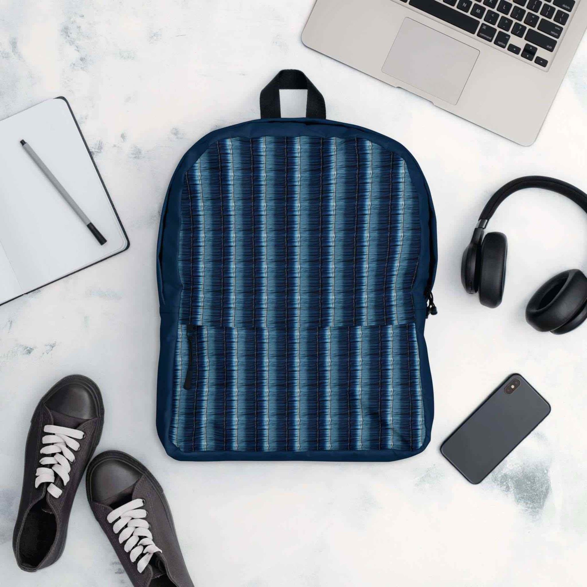 Flatlay of backpack surrounded by its possible contents - laptop, phone, headphone, writing pad, pen and even shoes.