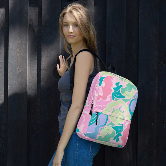 Caucasian woman with a backpack slung over her left shoulder, looking left to the camera. The backpack features an abstract floral design in predominantly soft pinks, and soft greens and blues. The woman stands in front of dark grey feature wall.