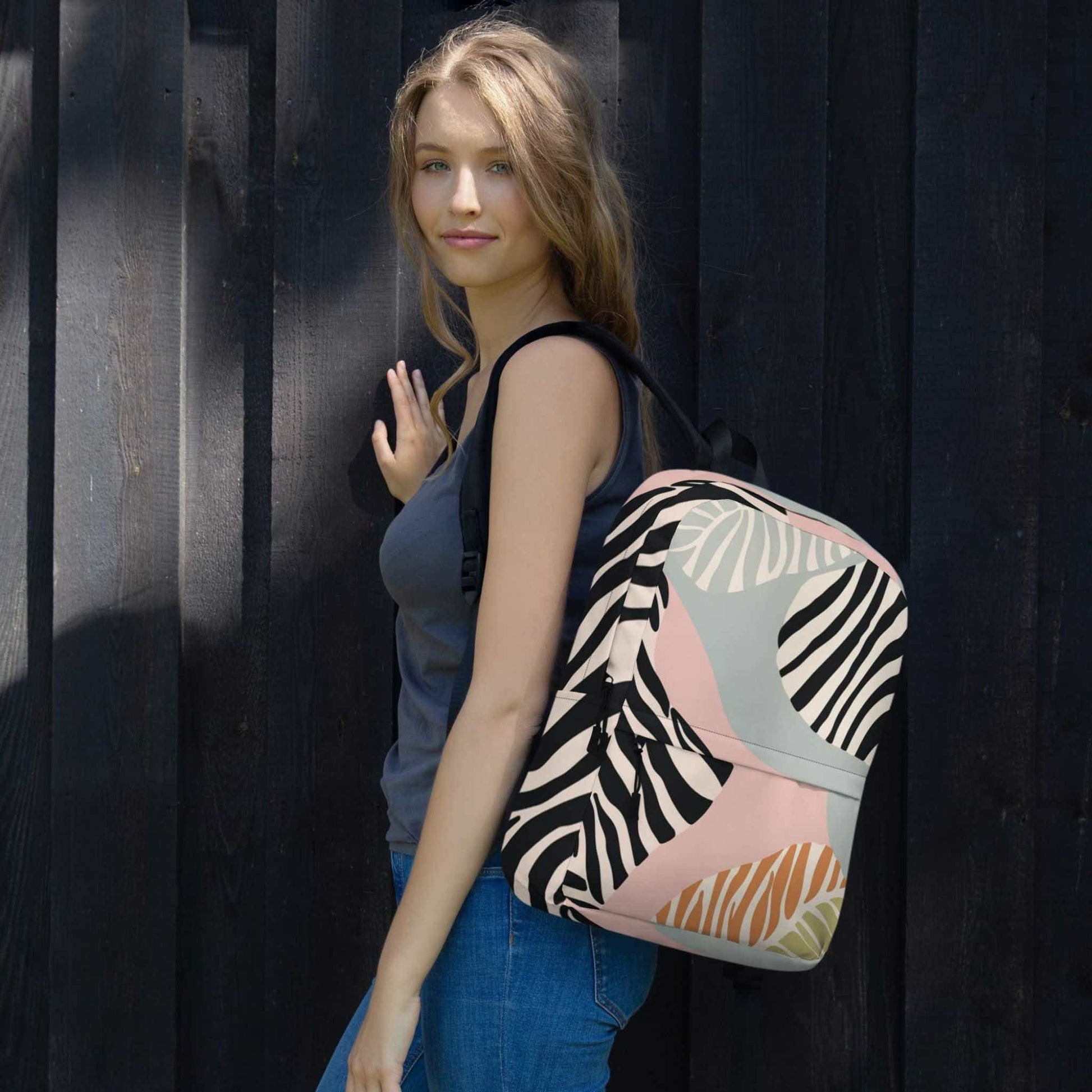 A zebra print backpack slung over her left shoulder of a woman. The backpack features a zebra inspired design with blacks, soft pink, soft green and tan colours. 