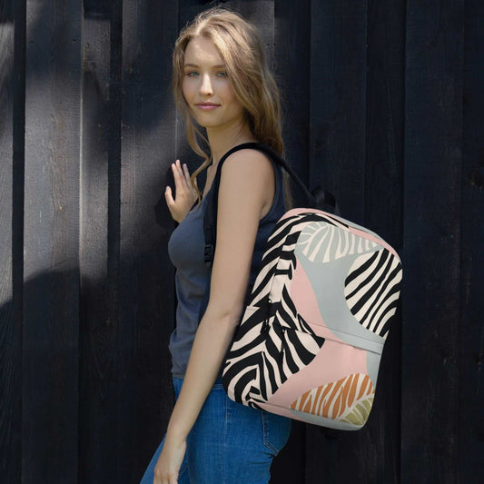 A zebra print backpack slung over her left shoulder of a woman. The backpack features a zebra inspired design with blacks, soft pink, soft green and tan colours. 