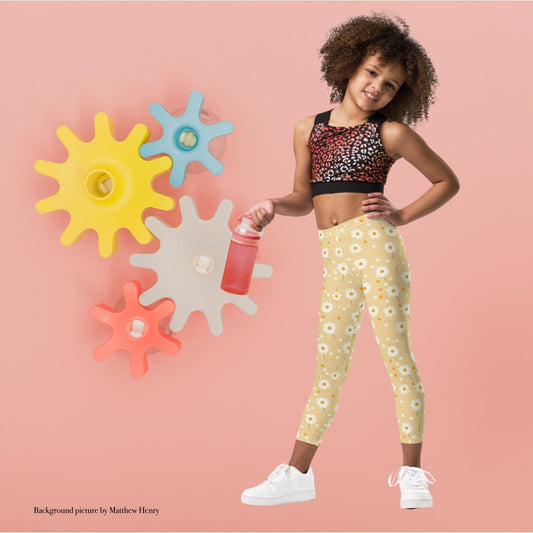 2T yellow leggings named DAISYDOODLE for toddlers, and bigger sizes for kids. This design features playful daisies &amp; polka dots on a bright egg yellow background, worn by a young girl against a pink background with colotful cogs.