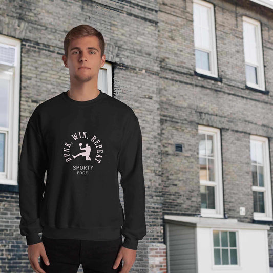 Basketball sweatshirt in black color, with the words "Dunk", "Win", "Repeat" and "Sporty Edge" circulating a graphic of a basketball player in action, worn by a man sanding in front of a classic brick building.