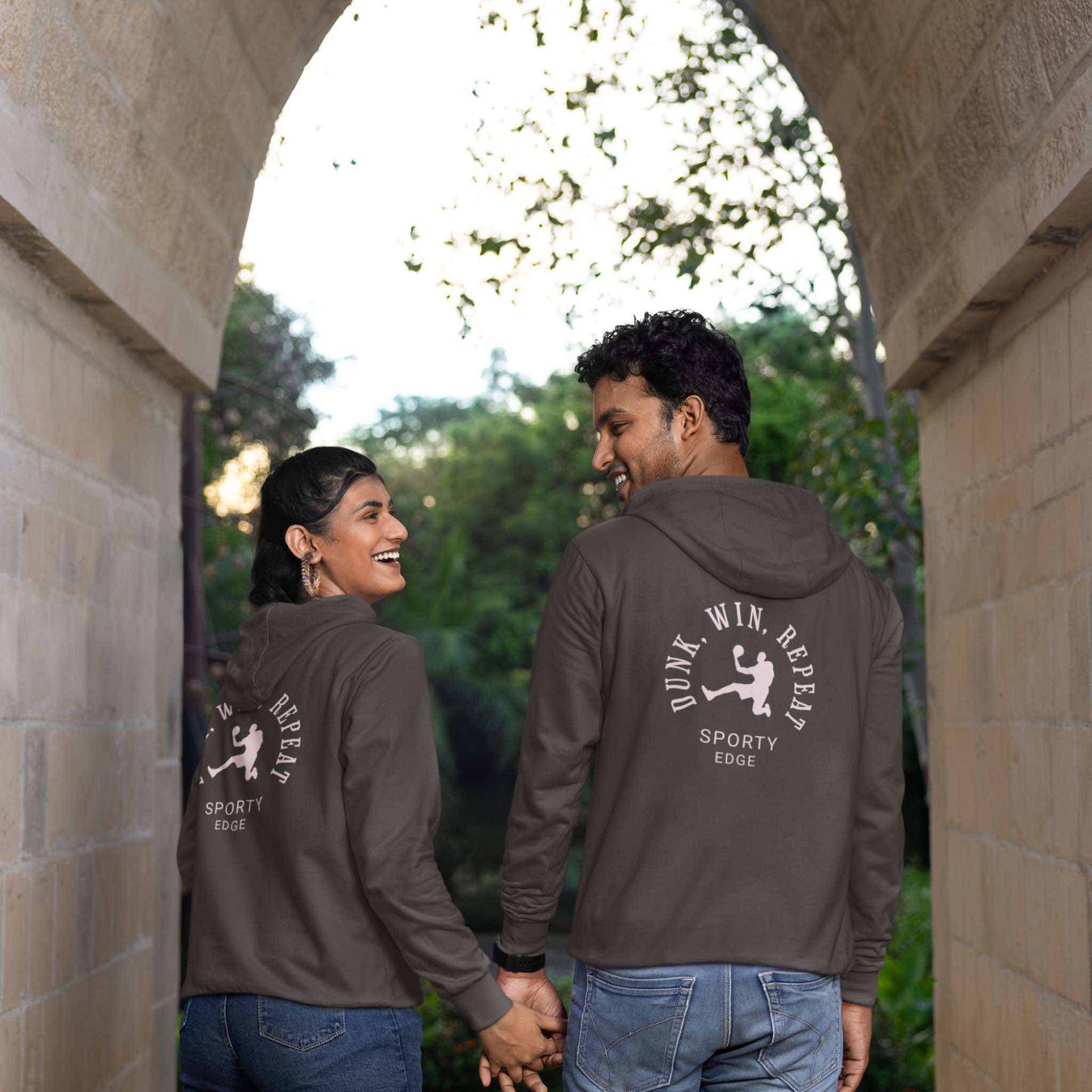 ack view of man and woman holding hands wearing matching charcoal heather cotton basketball hoodies under an arch.