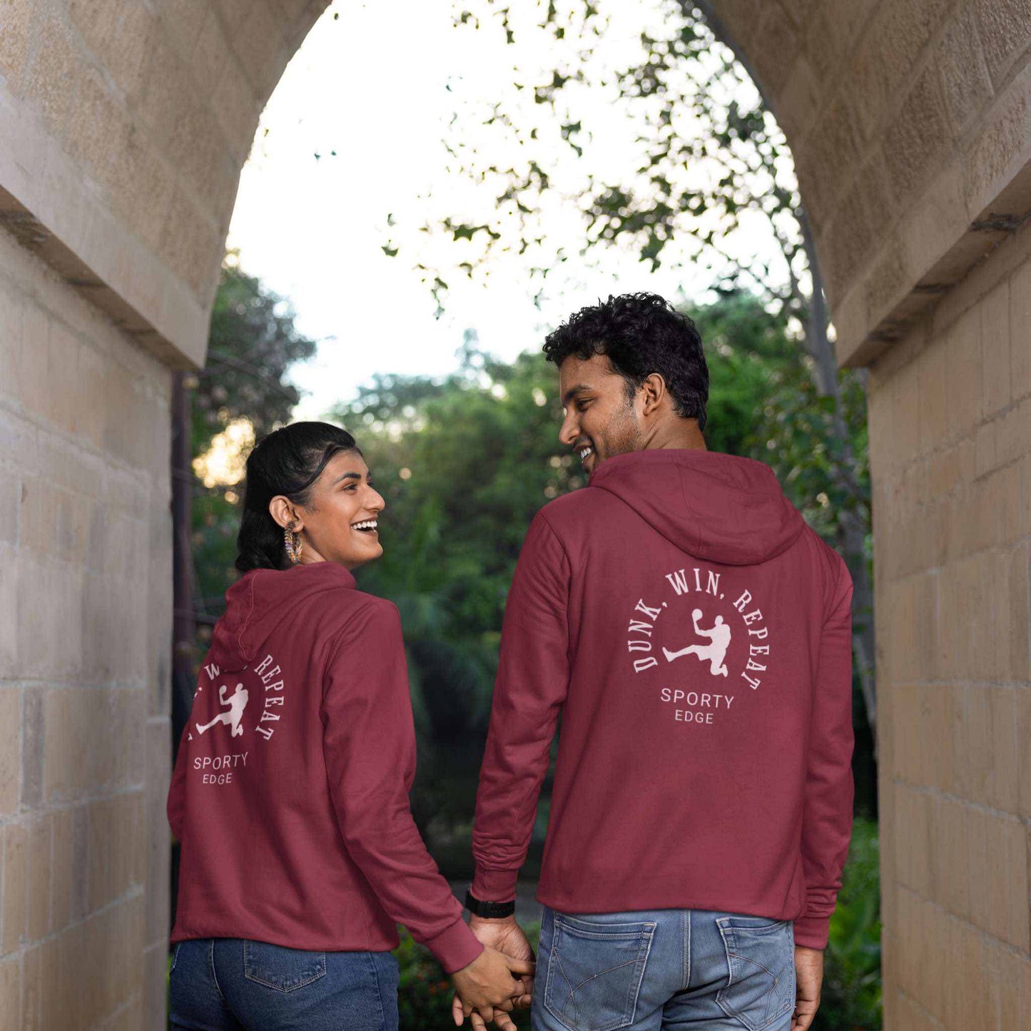 ack view of man and woman holding hands wearing matching maroon cotton basketball hoodies under an arch.