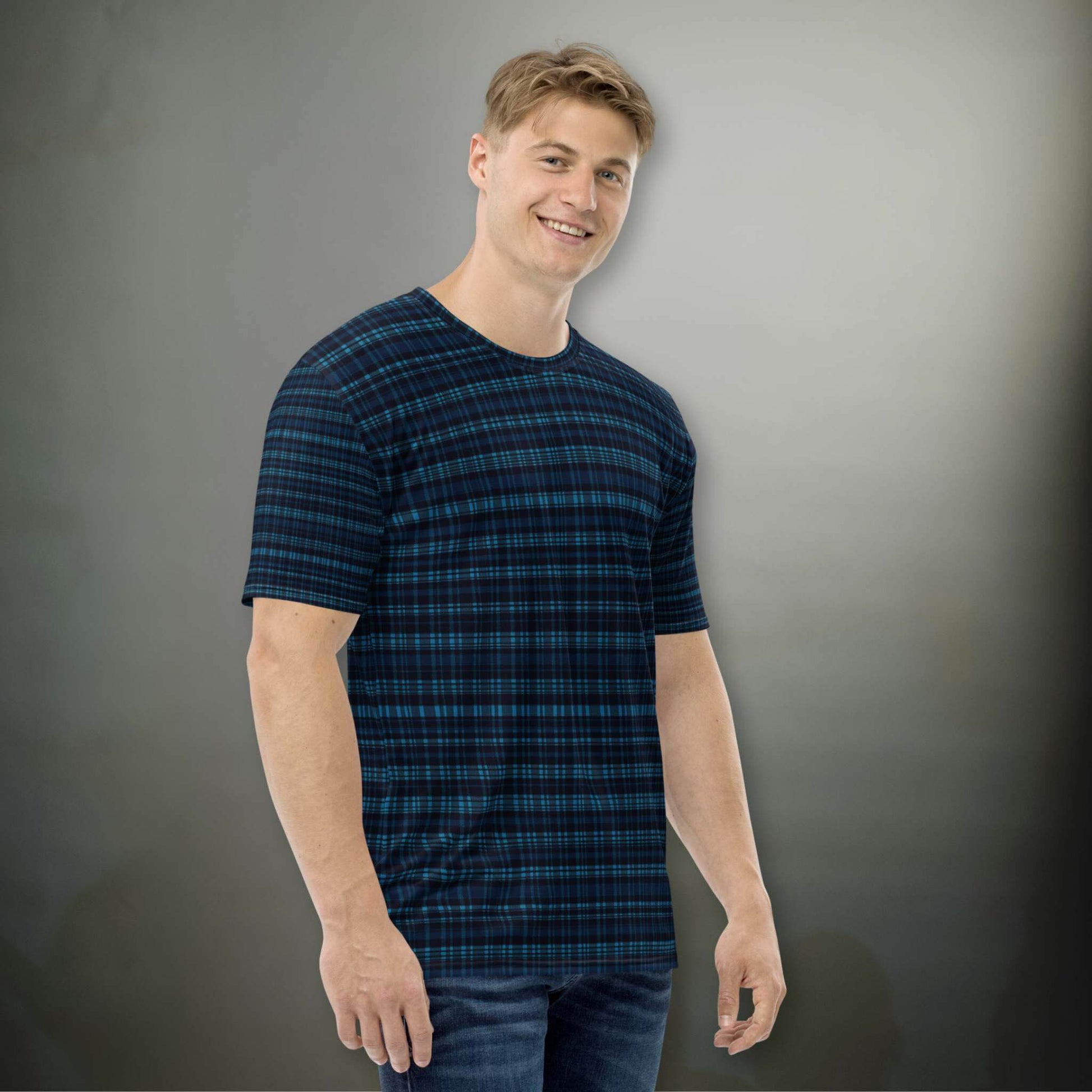 Male Caucasion in a plaid dark blue all-over-print tshirt, in a plaid design that blends modern structure with timeless charm, offering a sophisticated yet versatile look. The man stands in front of an illuminated dark grey wall.