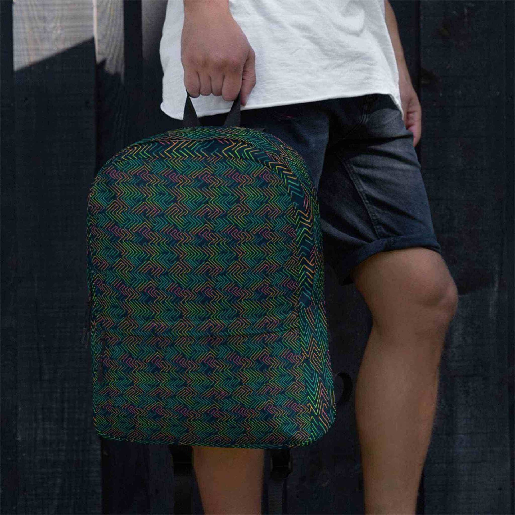 Close up view of backpack with dark neon pattern akin to electric circuits held by a man wearing bermudas. Style of backpack is athletic and urbane.