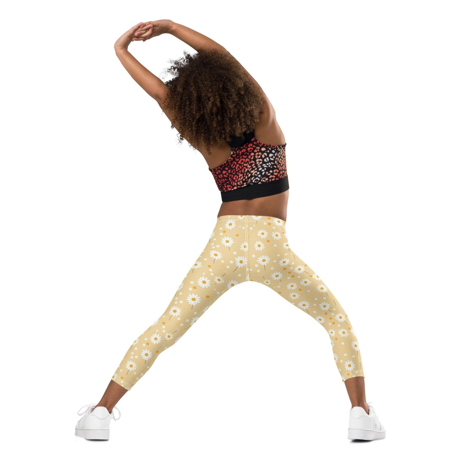 Back view of a black gril wearing a crop top, and leggings which features sweet daily print on an egg yellow background.  The gris's hands and legs are stretched out as she exercises.