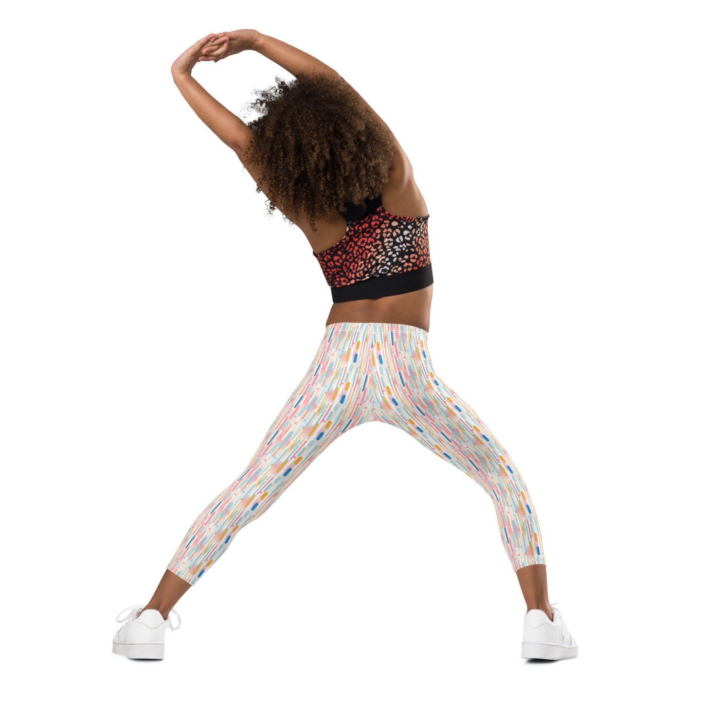 Back view of a black gril wearing a crop top and leggings which features playful candy colored lines in a white background. The girl's hands and legs are stretched out as she exercises.