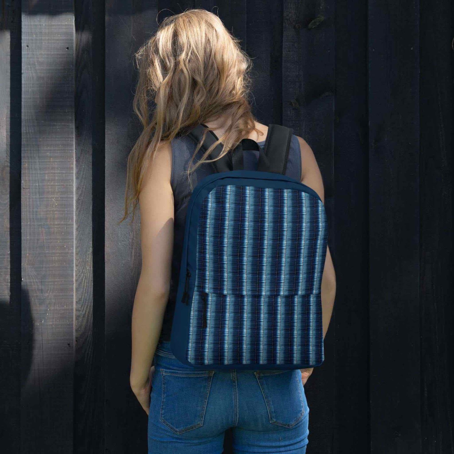 Rear view of a woman wearing a denim stripe backpack. The woman is facing a dark feature wall.