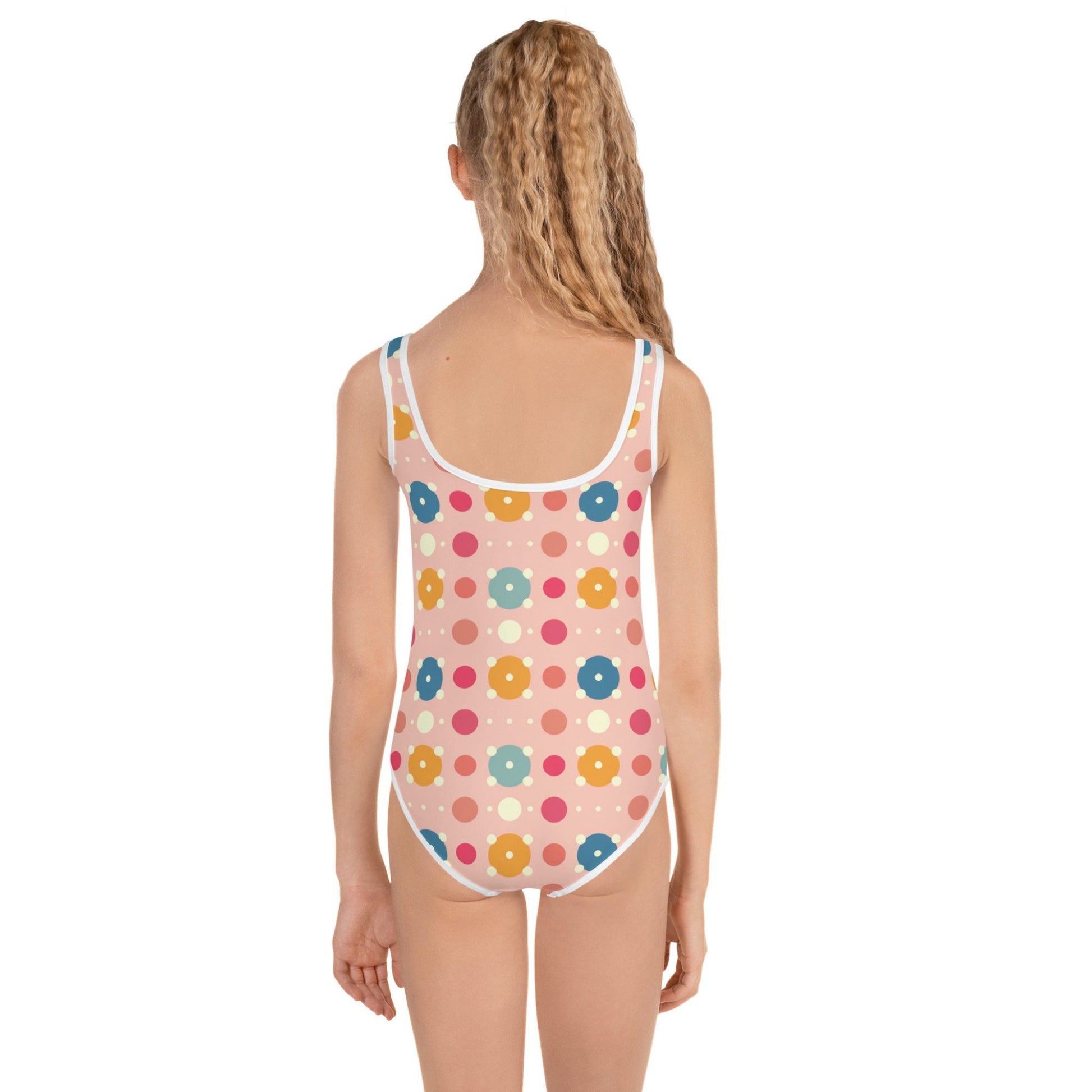 Cute infant swimsuit, suitable for kids in general, features a playful pattern of pastel and white circles on a pink background, worn by a young girl, her back facing the camera. White background.
