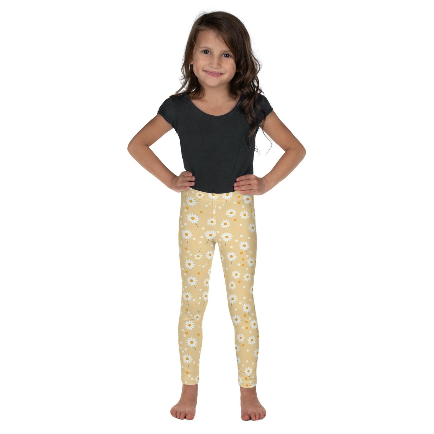 Front view of a dark skinned gril wearing a black tshirt top, and leggings which feature sweet daisy prints on an yellow background. The girl has her arms folded on her side and is standing against a white background.