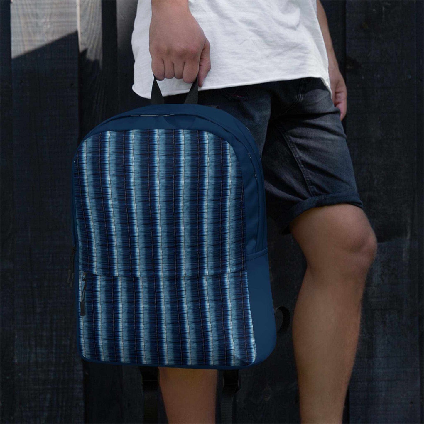 Close up view of denim stripe backpack held by a man wearing bermudas.