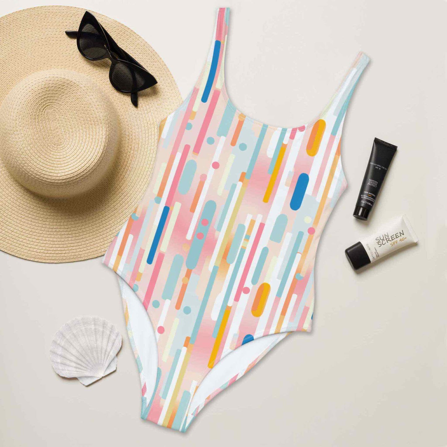 A flat lay of a light candy coloured one-piece swimsuit, front side facing up. A hat, sunglasses, seashell and tubes of sun screen creams lying next to it.