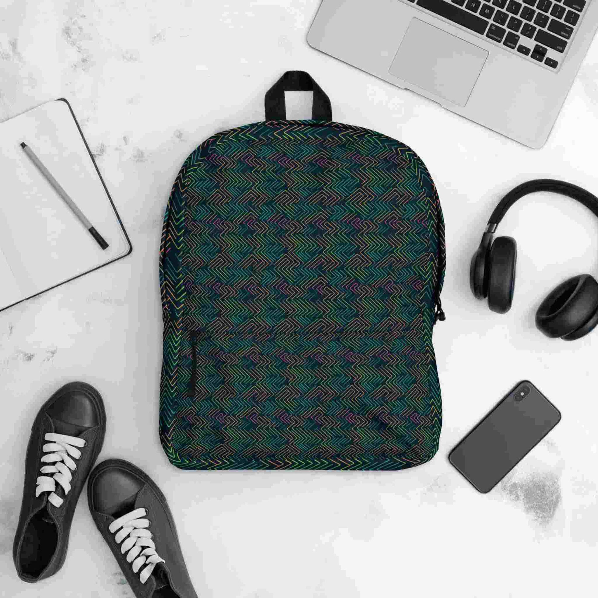 Flatlay of a printed backpack, featuring a dark neon electrical circuit design, surrounded by items it could possibly contain, including a laptop, handphone, headphone, note pad and pen, and even shoes.