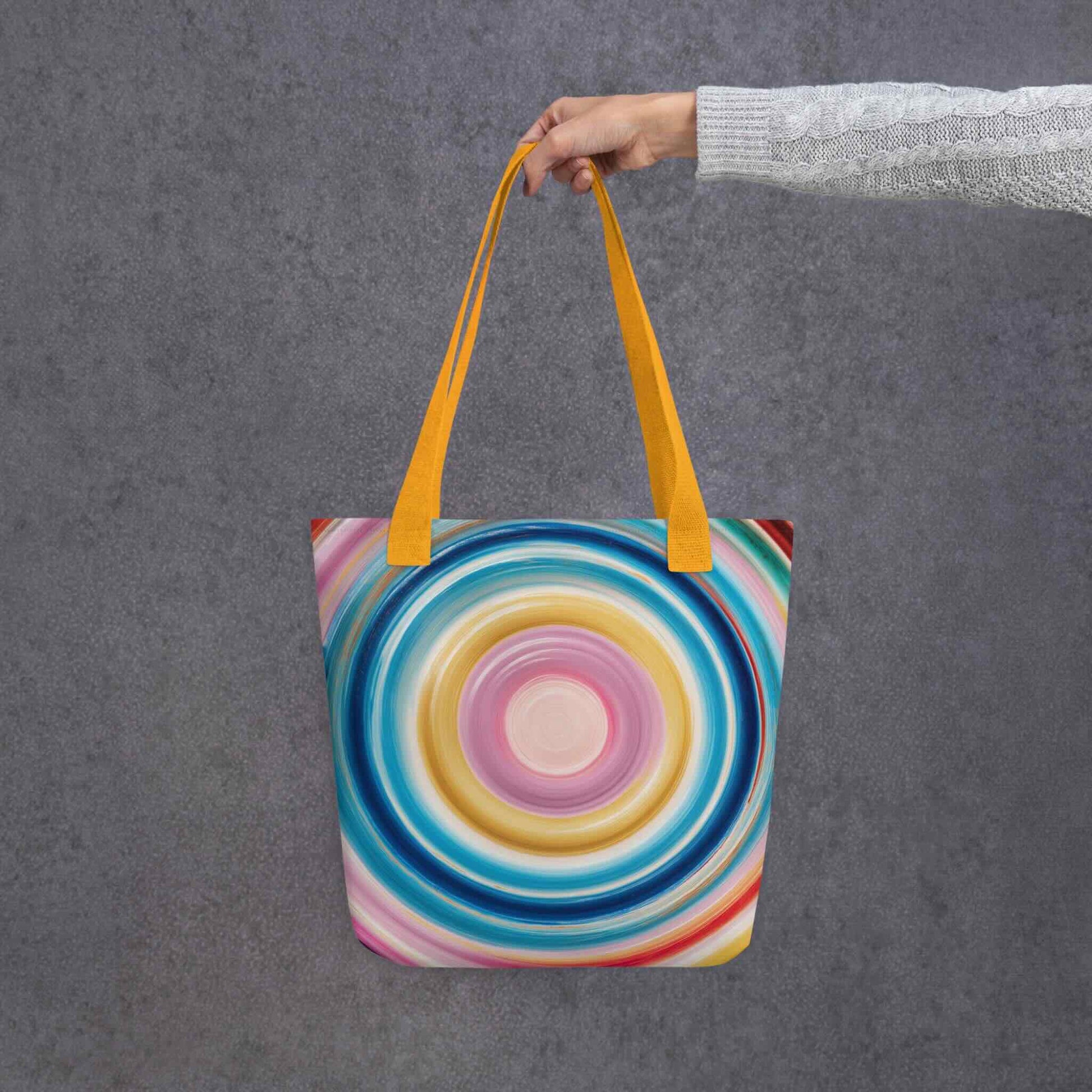 Colorful tote bag which features a mesmerizing abstract design of strong, hypnotic color circles, with yellow handles. Dimension 15x15 inches, polyester. Grey blackground. 