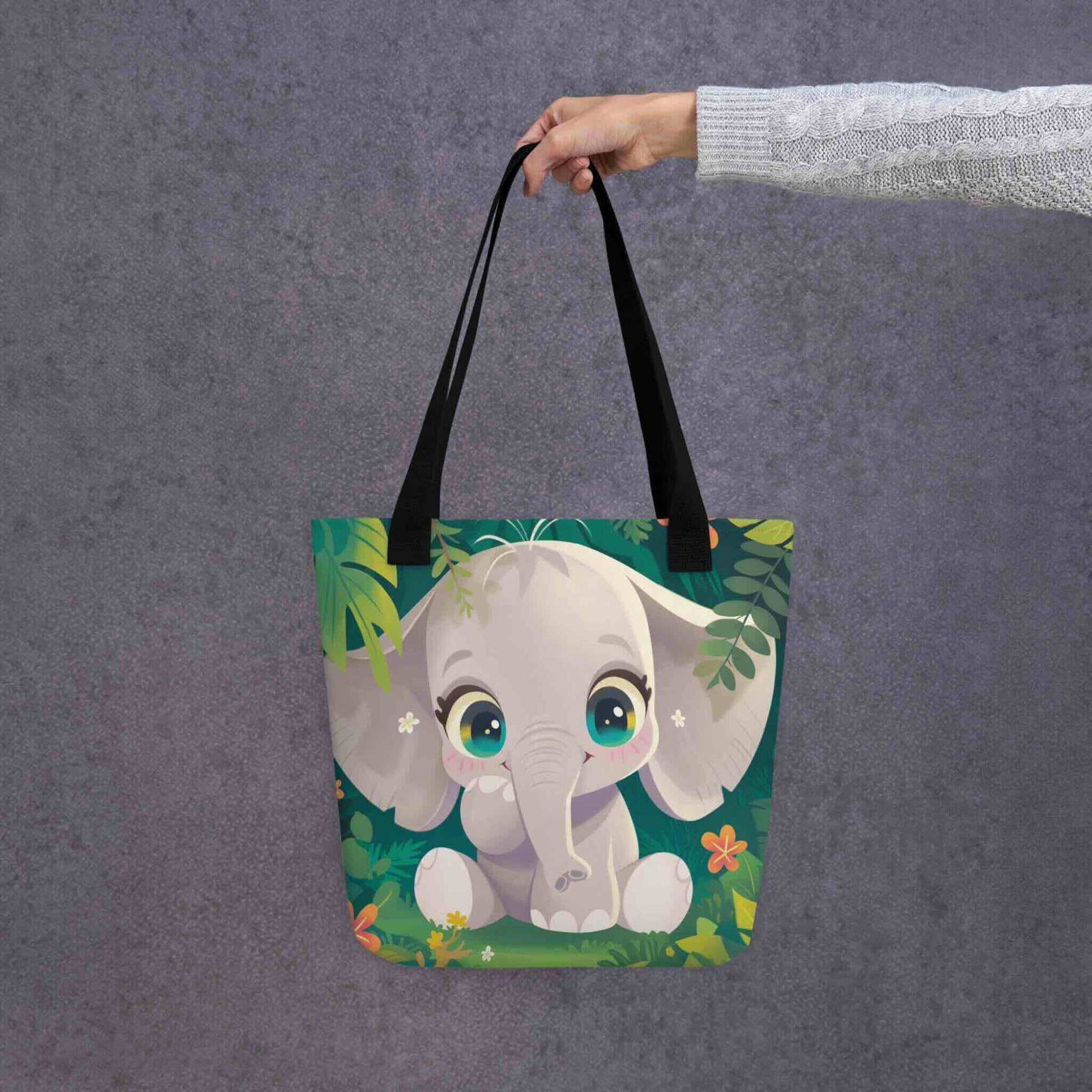 Cute Elephant Tote Bag, design which features a warm, charming baby elephant, with black handles, held in a hand. 15x15 inches. Grey background.