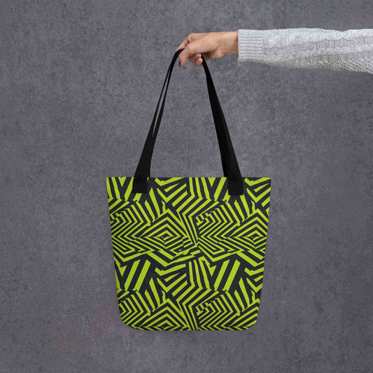 An avant garde tote bag with black handles, which features bold black and green op art illusion, held in a lady's hand. Size is 15x15 inch. Grey background.