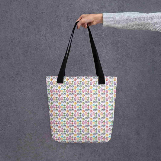A fruit tote bag with black handles, which features a colourful cheerful doodles of fruits in a crisp white background, held in a lady's hand. Dimension 15x15 inches. Grey background.