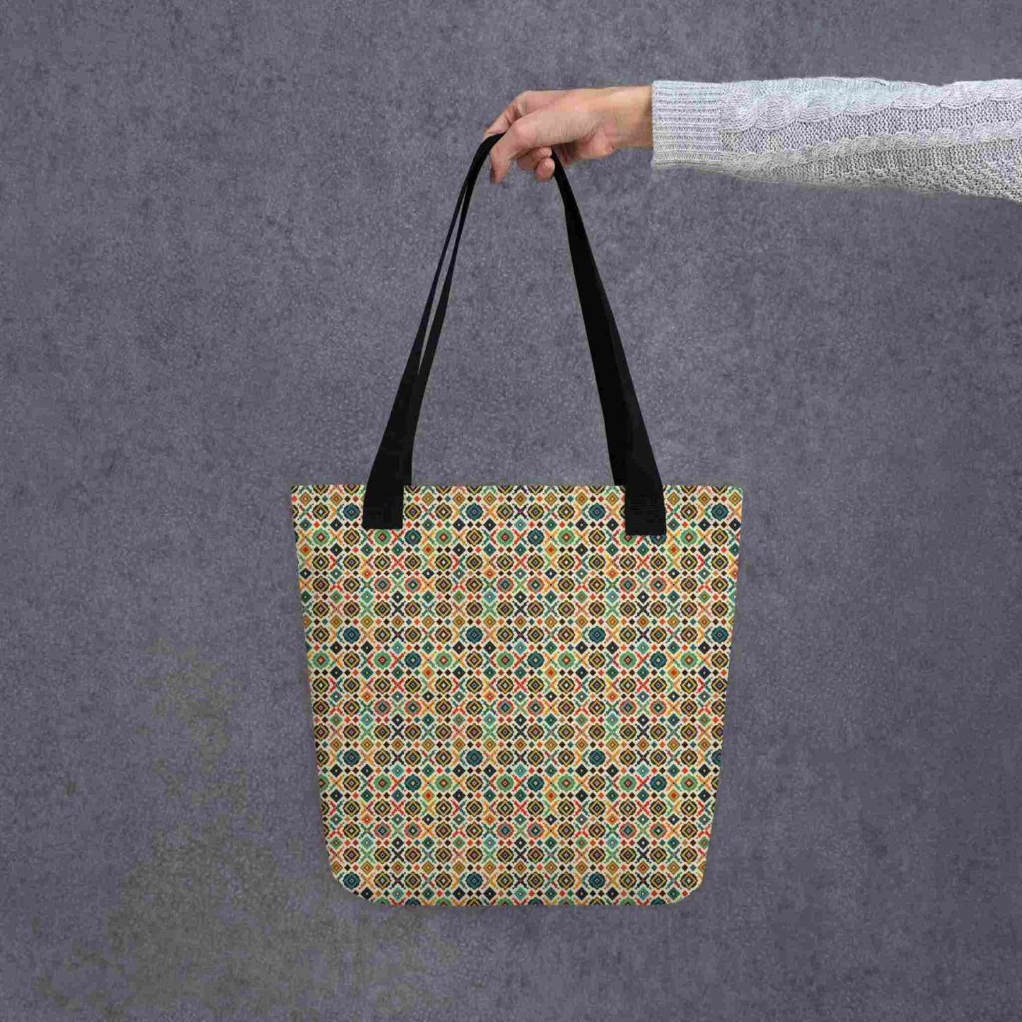 A 15x15 inch tote bag with black handles, which design is an Argentinian inspired diamond pattern, held by a lady's hand. Grey background.