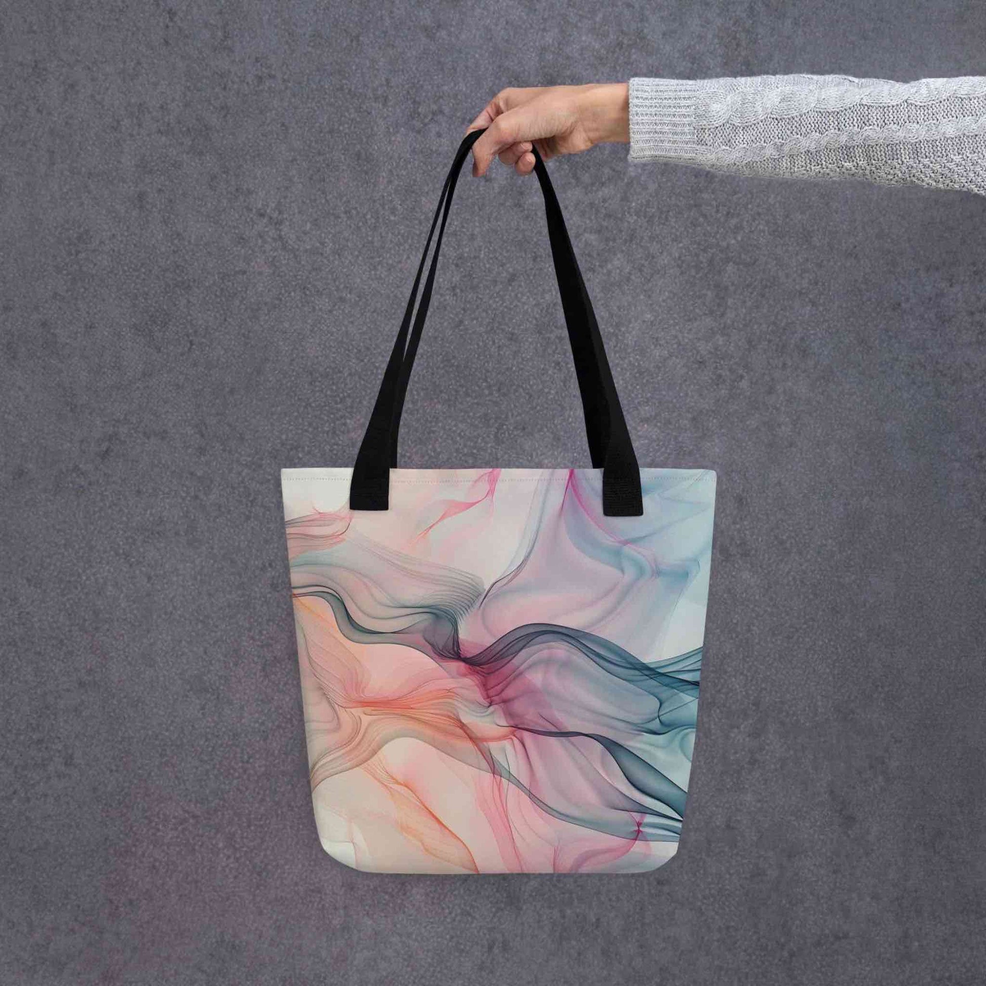 Fashion ladies tote bag with black handles, which design features an abstract art of artistic wavy bluish and pastel lines, held by a lady's hand. Dimension 15x15 inches. Grey background.