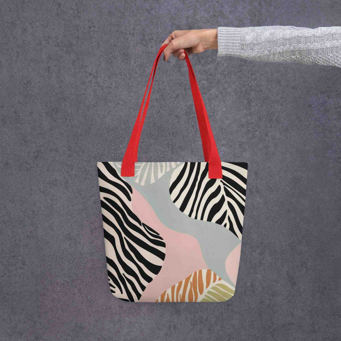 A 15x15 inch tote bag with red handles, in a colourful Zebra inspired design, held in a lady's hand. Grey background.