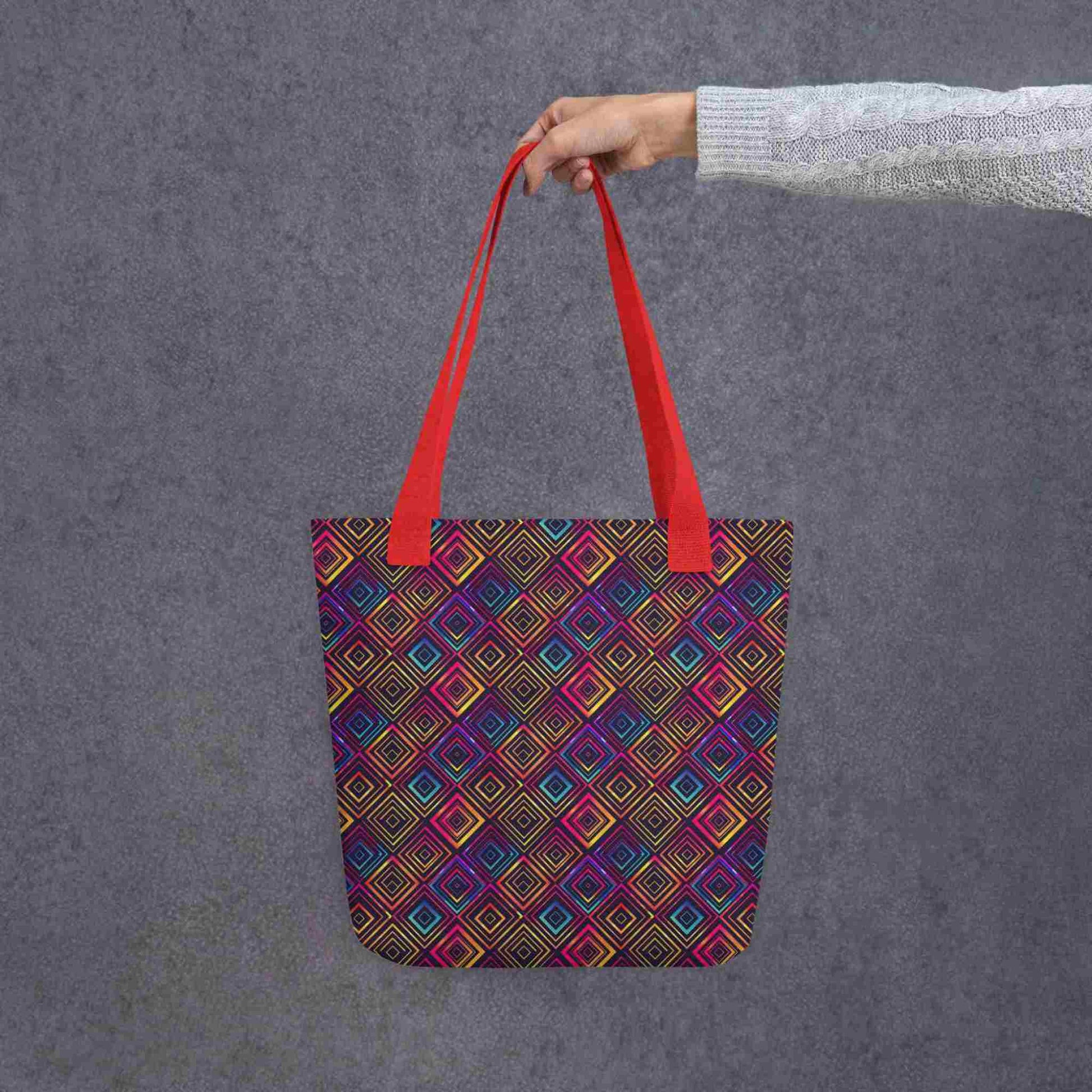 Fashion tote bag with red handles, which features a neon tapestry design in a sophisticated blend of colors, held by a lady's hand. Dimension 15x15 inches. Grey background.