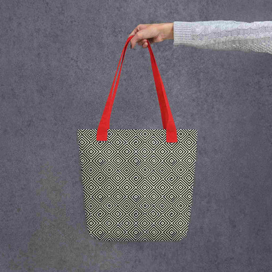 Diamond pattern tote bag with red handle, a mesmerizing black and white geometric ook, held in a lady's hand against a grey background.