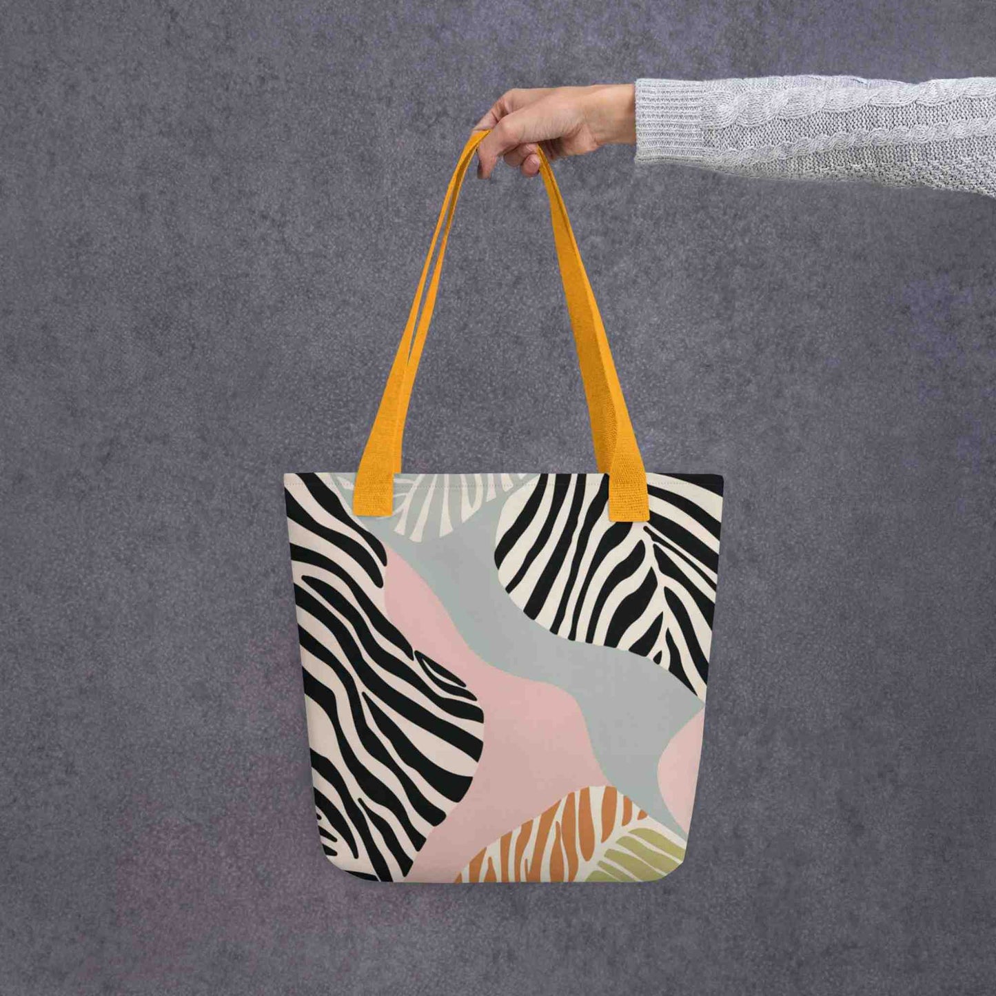 A 15x15 inch tote bag with yellow handles, in a colourful Zebra inspired design, held in a lady's hand. Grey background.