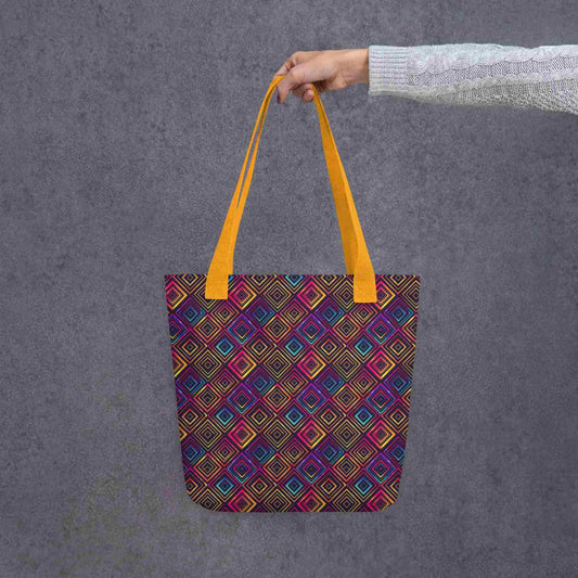 Fashion tote bag with yellow handles, which features a neon tapestry design in a sophisticated blend of colors, held by a lady's hand. Grey background.